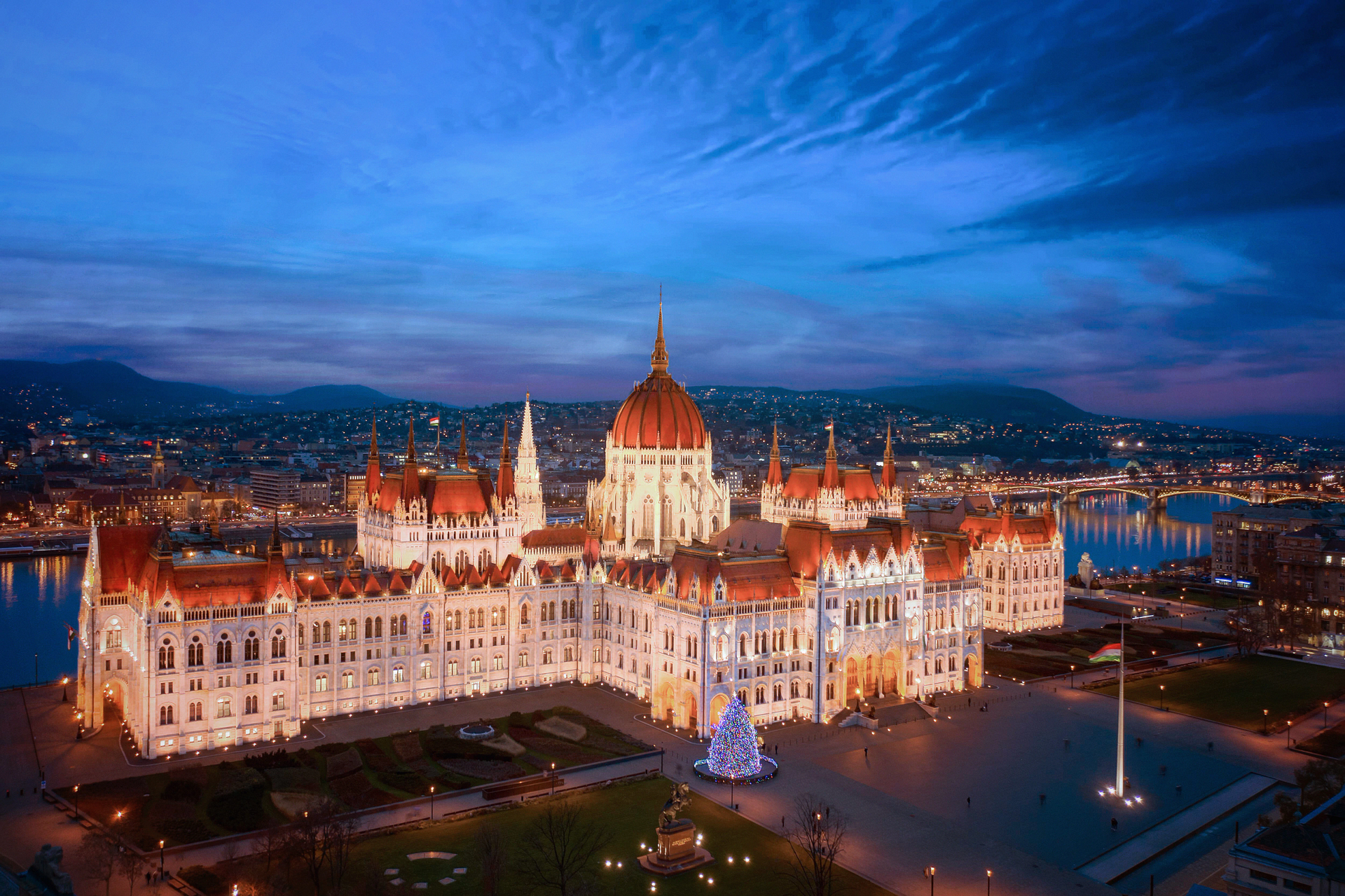 Hungarian Parliament Building at dusk, illuminated in white and gold against a blue sky.