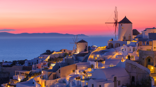 A sunset over a small town with windmills and buildings.