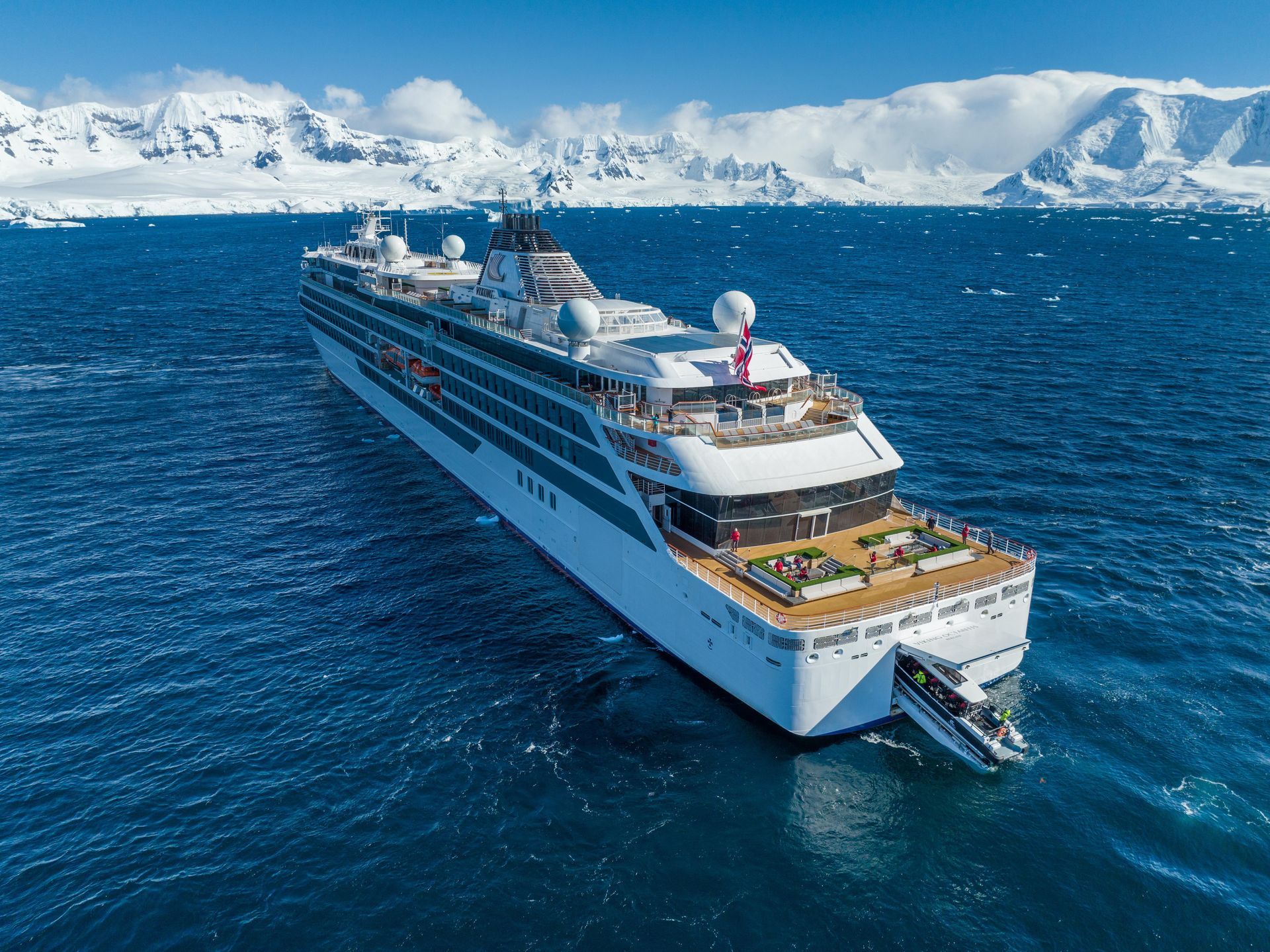 White cruise ship sailing on blue water near snowy mountains.