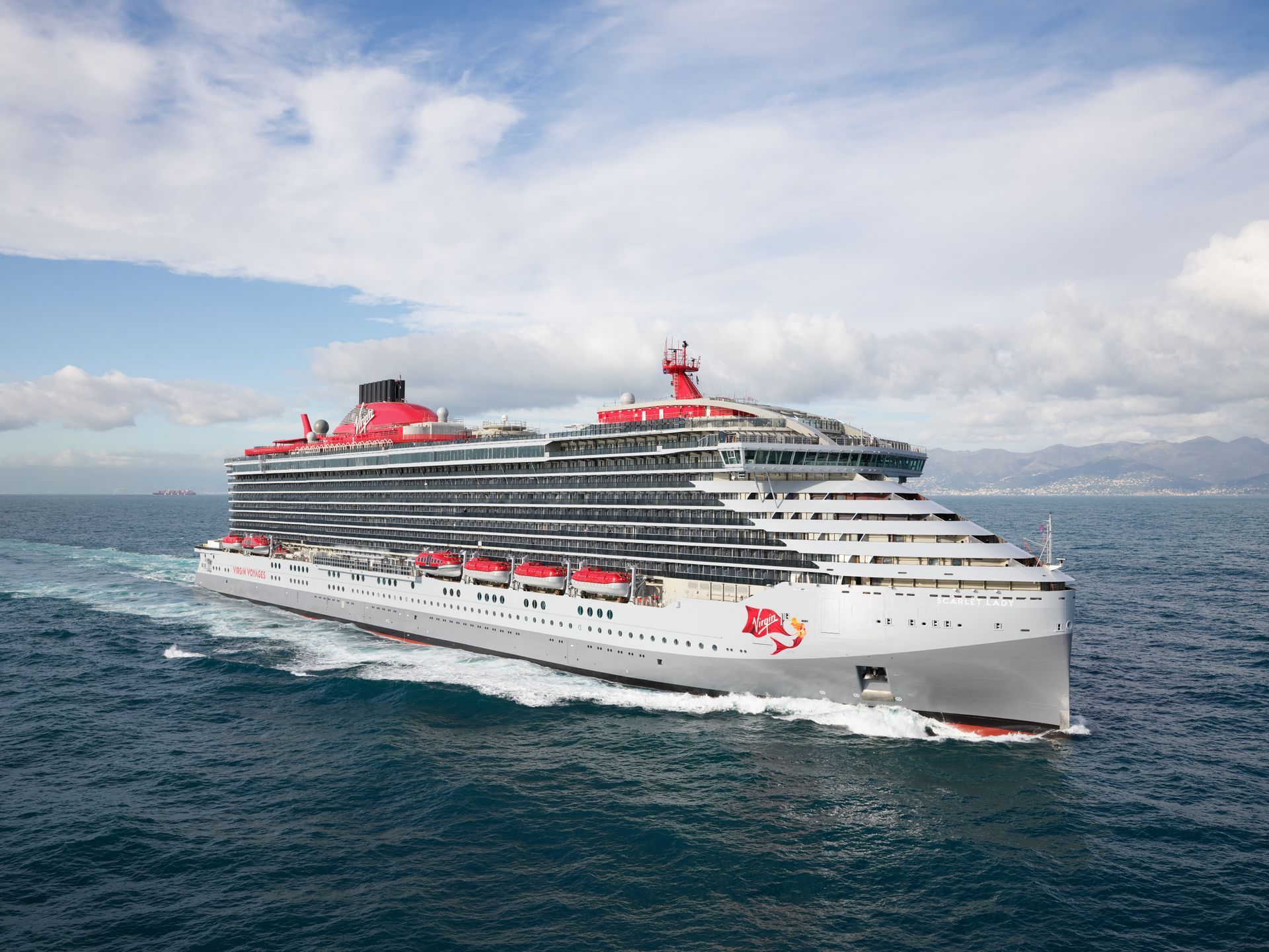 A large, red and white Virgin Voyages cruise ship sailing on the ocean.