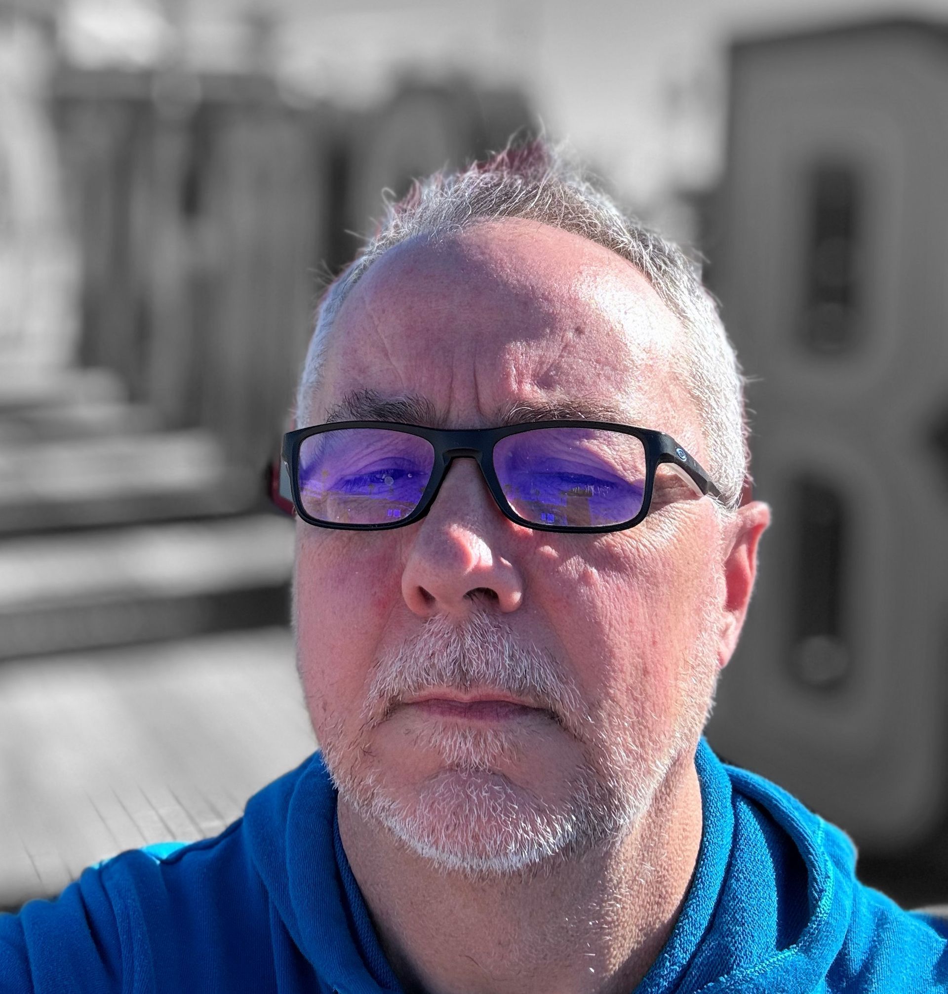 Man with glasses, graying hair, blue shirt, outdoors. Selective color.