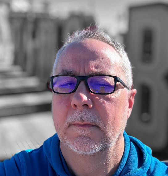 Man with glasses, graying hair, blue shirt, outdoors. Selective color.