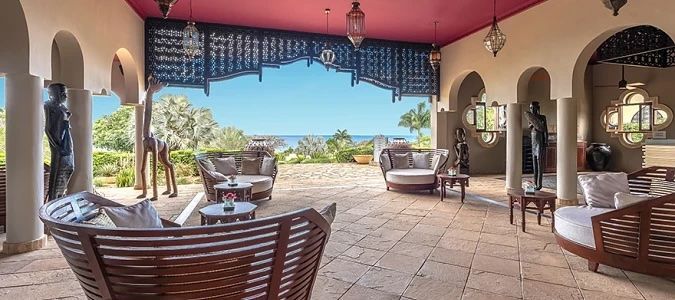 An outdoor lounge with a view of the ocean. Features curved sofas, sculptures, and arched architecture.