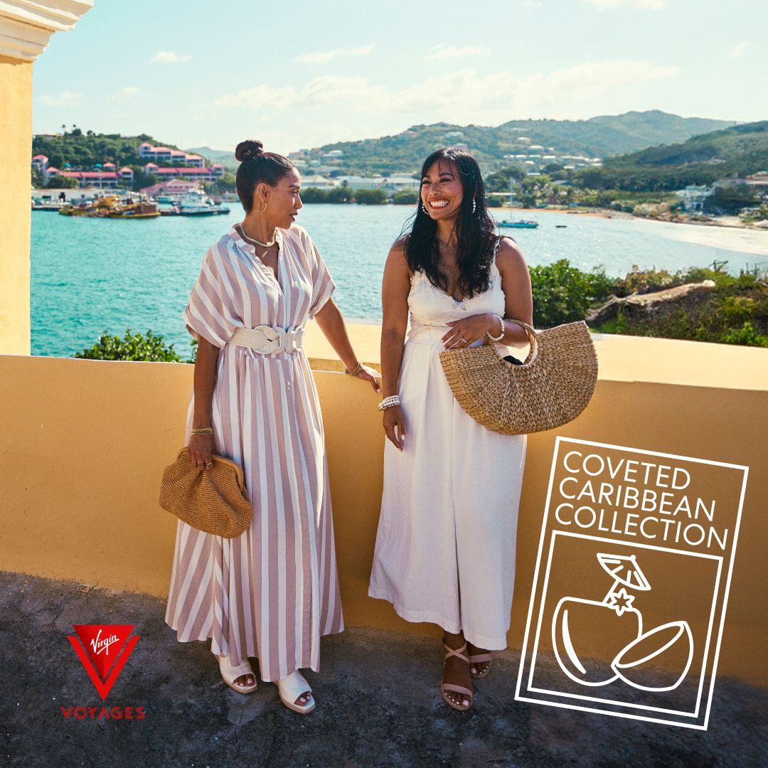 Two women on a balcony overlooking the sea. One wears a striped dress, the other a white dress. 