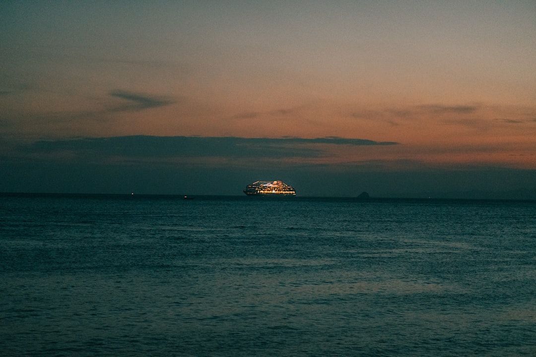 Ocean at dusk with a distant, illuminated ship; orange and blue sky reflecting on the water.