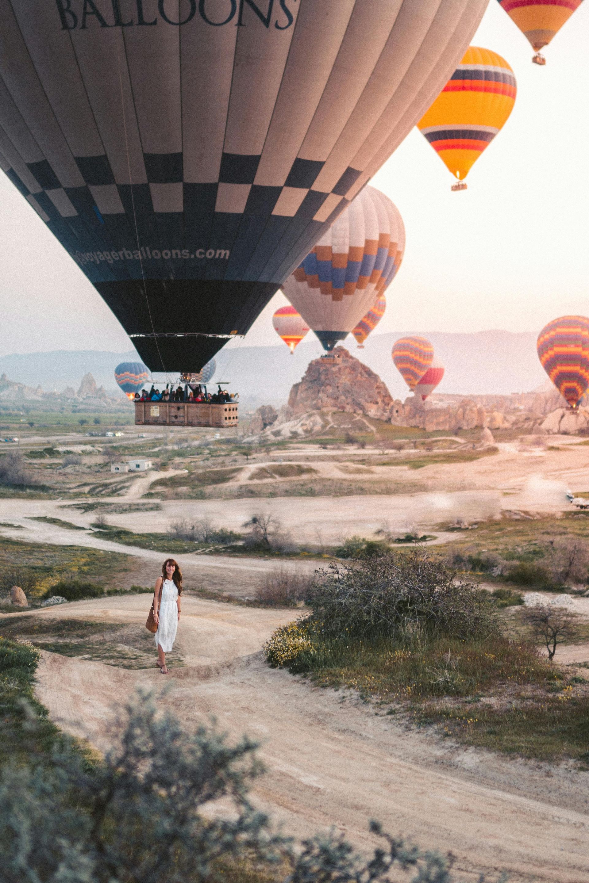 A woman is walking down a dirt road in front of a field of hot air balloons.