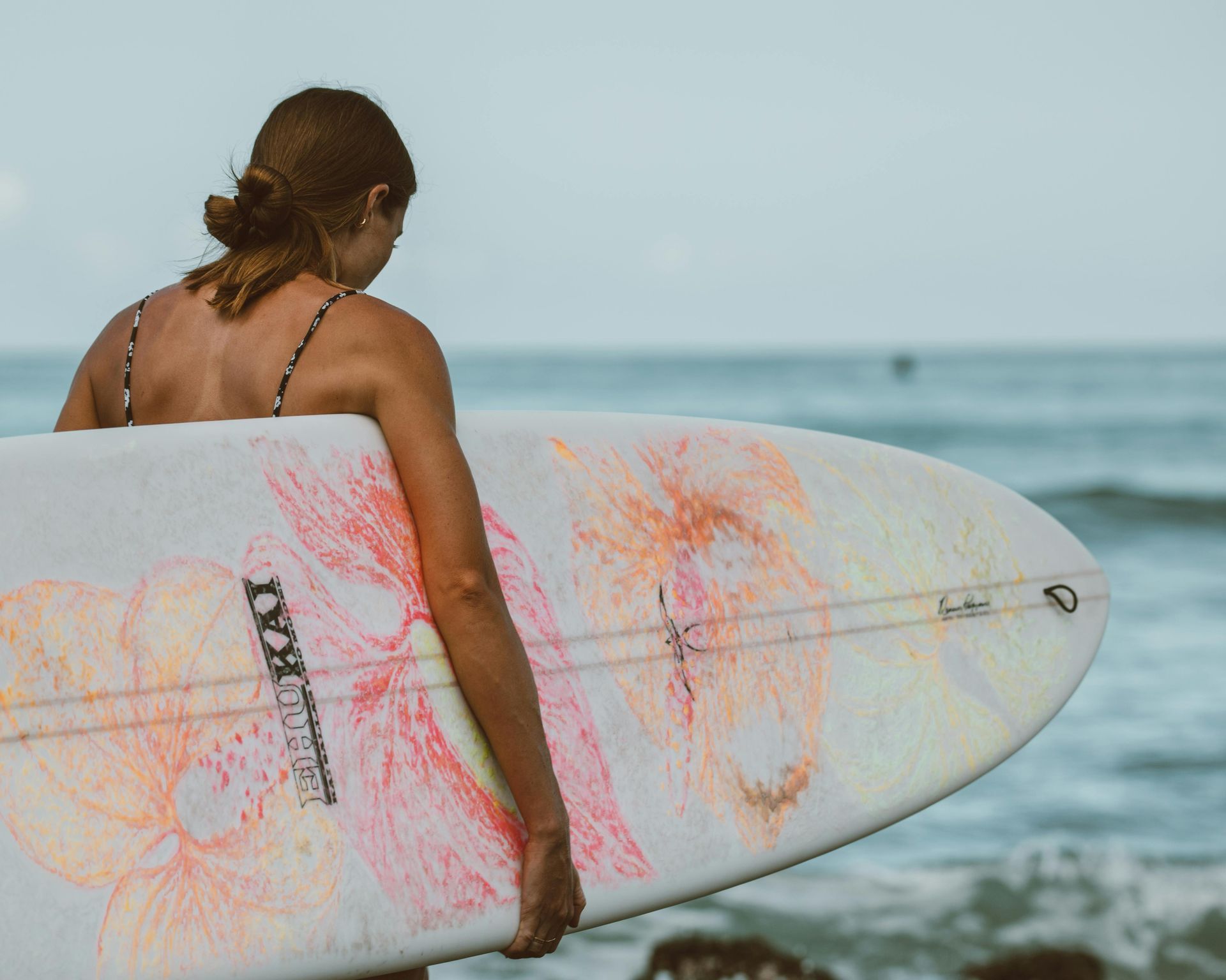 Woman carrying a surfboard toward the ocean, wearing a swimsuit.