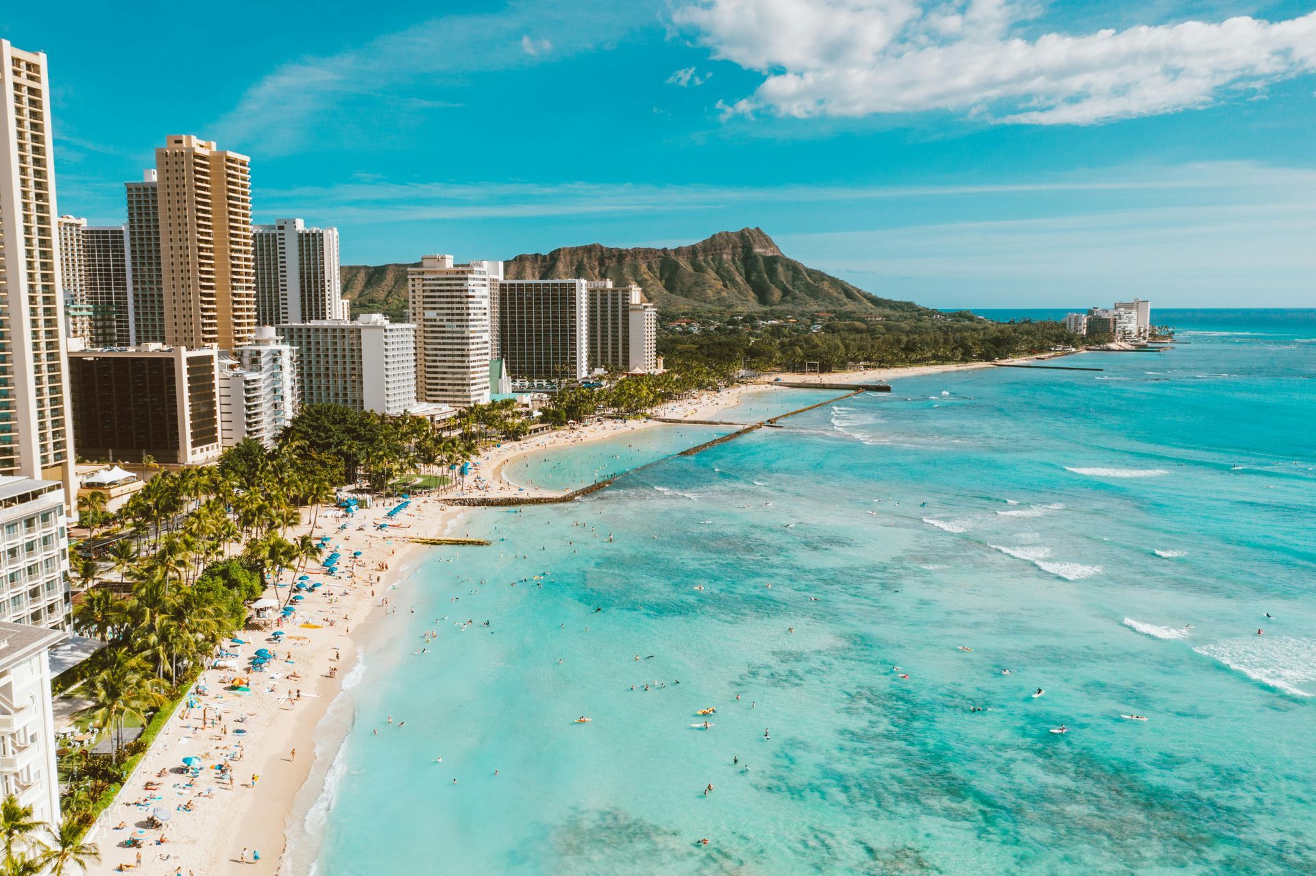 Waikiki Beach with buildings, ocean, Diamond Head, and people enjoying the sunny day.