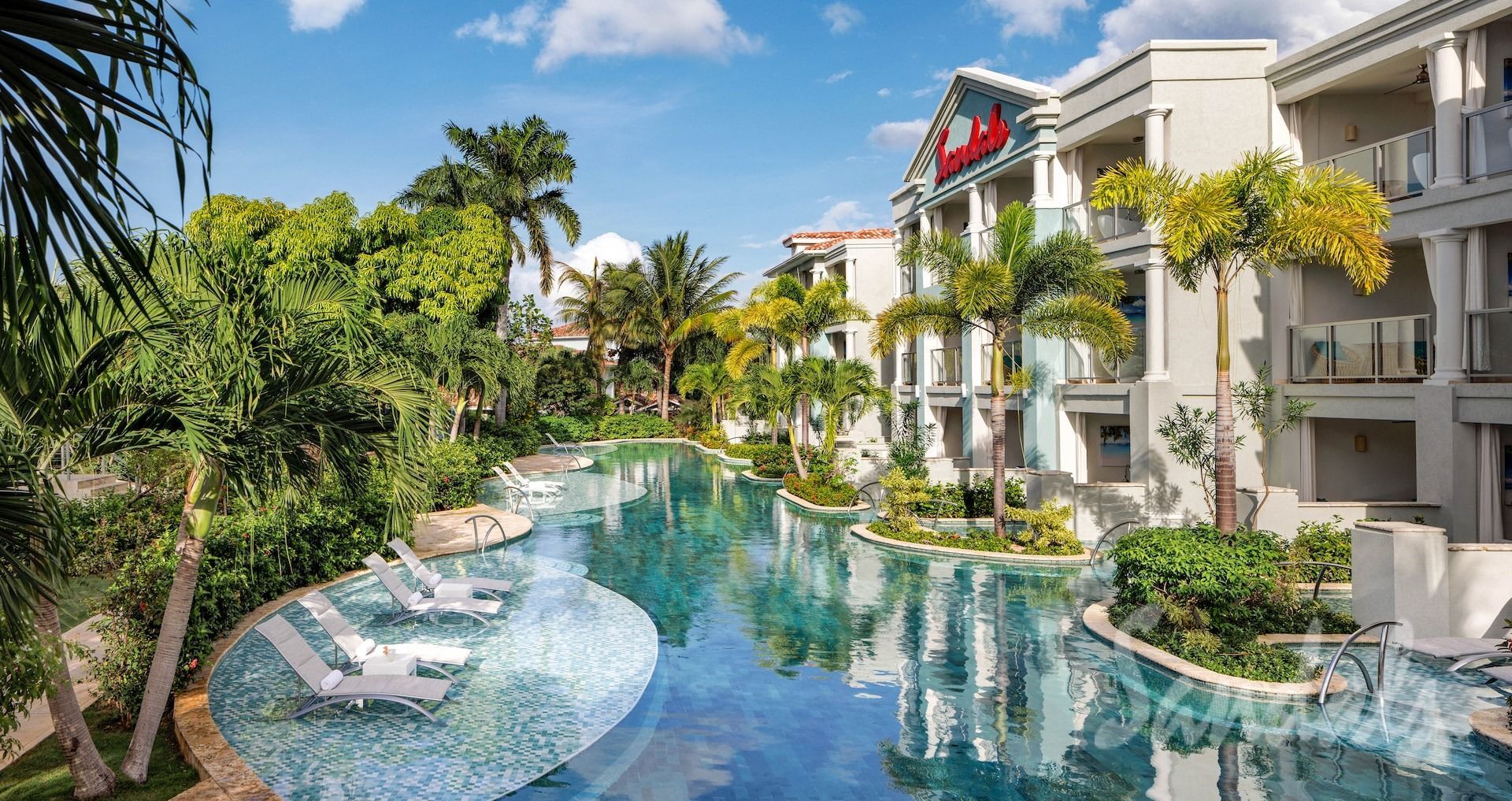 Luxury resort pool with blue water, lounge chairs, palm trees, and white villas under a sunny sky