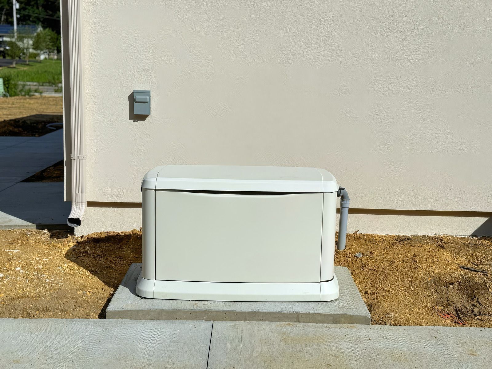 A beige generator on a concrete pad beside a light tan wall with a gray electrical outlet.
