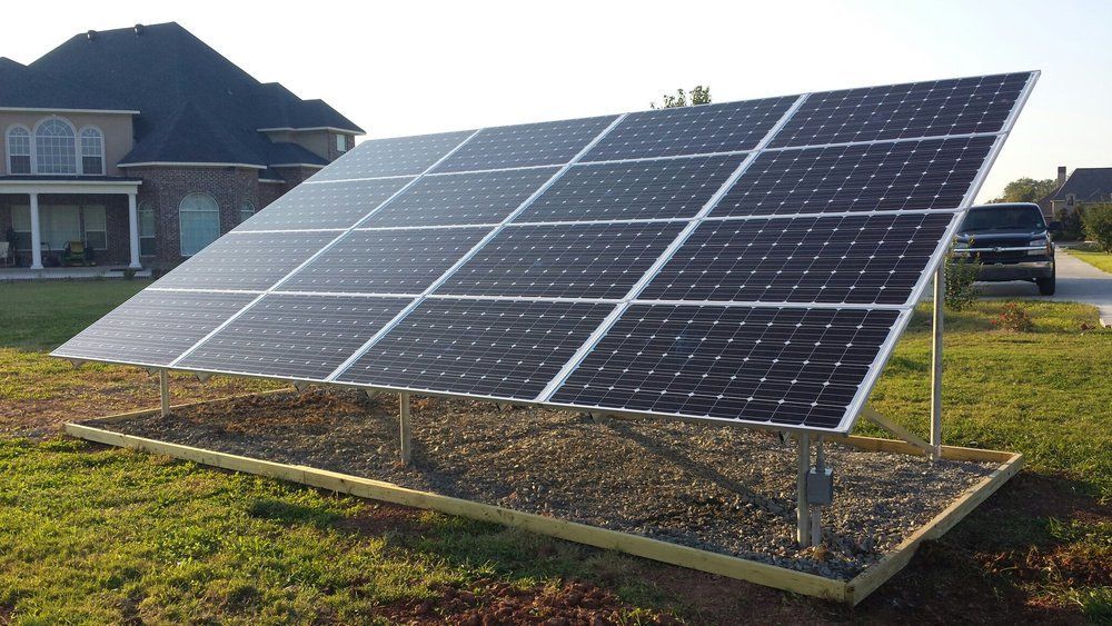 A row of solar panels are sitting in the grass in front of a house.