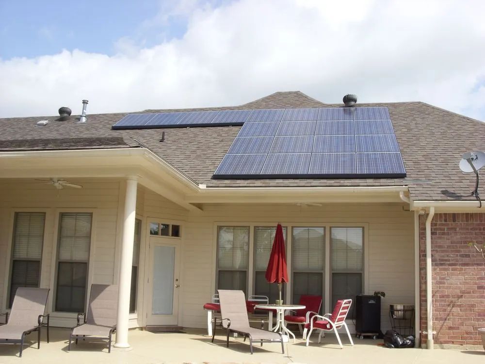 Solar panels installed on a residential roof above a patio with lounge chairs, a table, and an umbrella.
