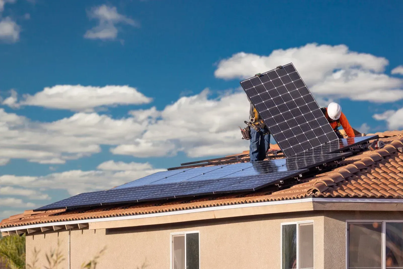 A man is installing solar panels on the roof of a house.