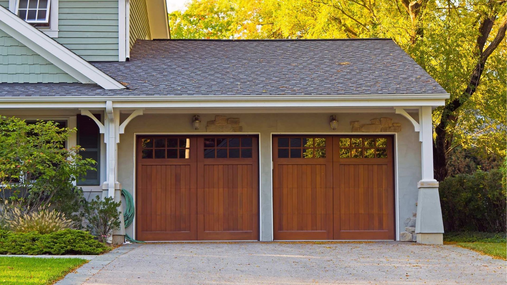 Two wooden carriage-style garage doors on a light-colored house exterior with surrounding trees.