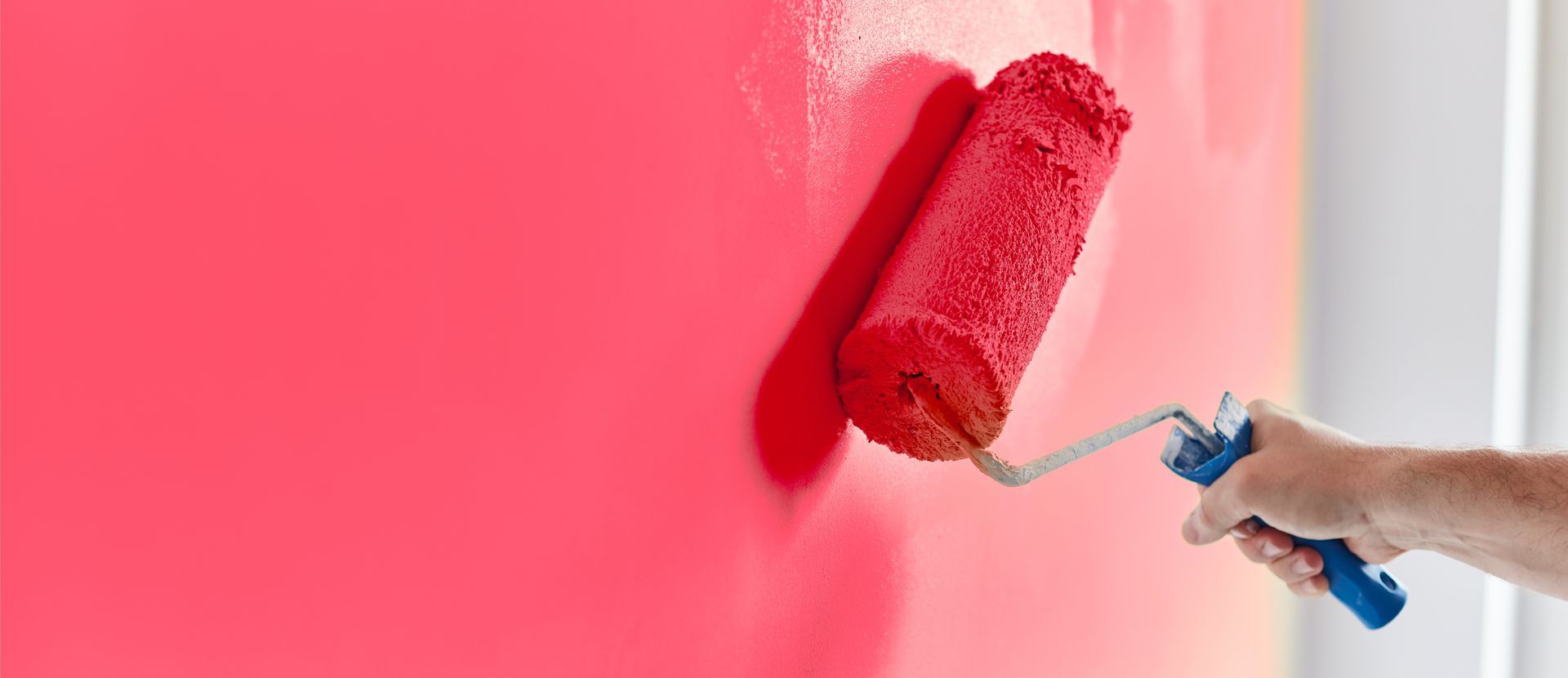 A person painting a wall red with a paint roller.