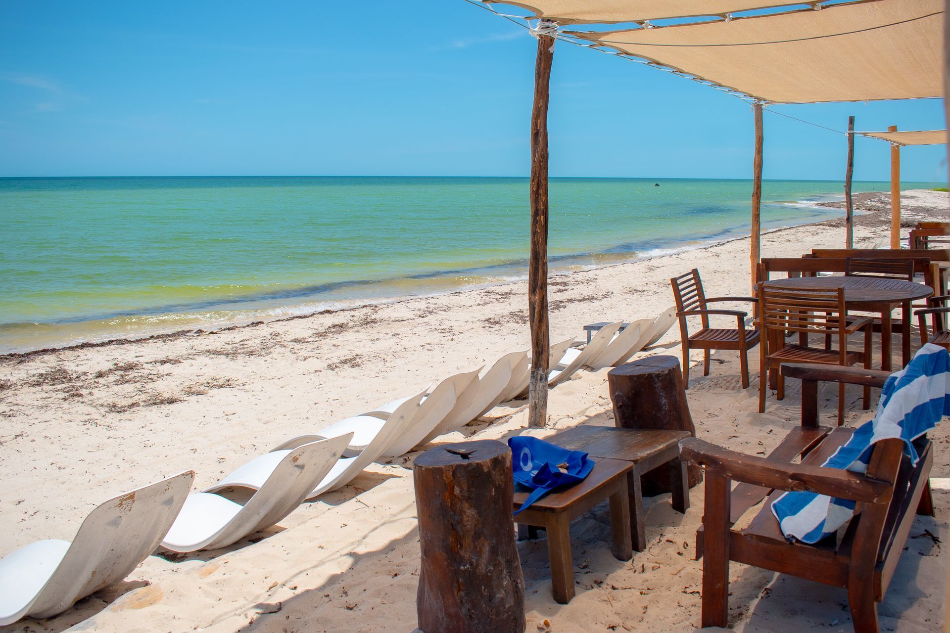 Una playa con sillas, mesas y sombrillas en un día soleado en Tecnohotel Beach