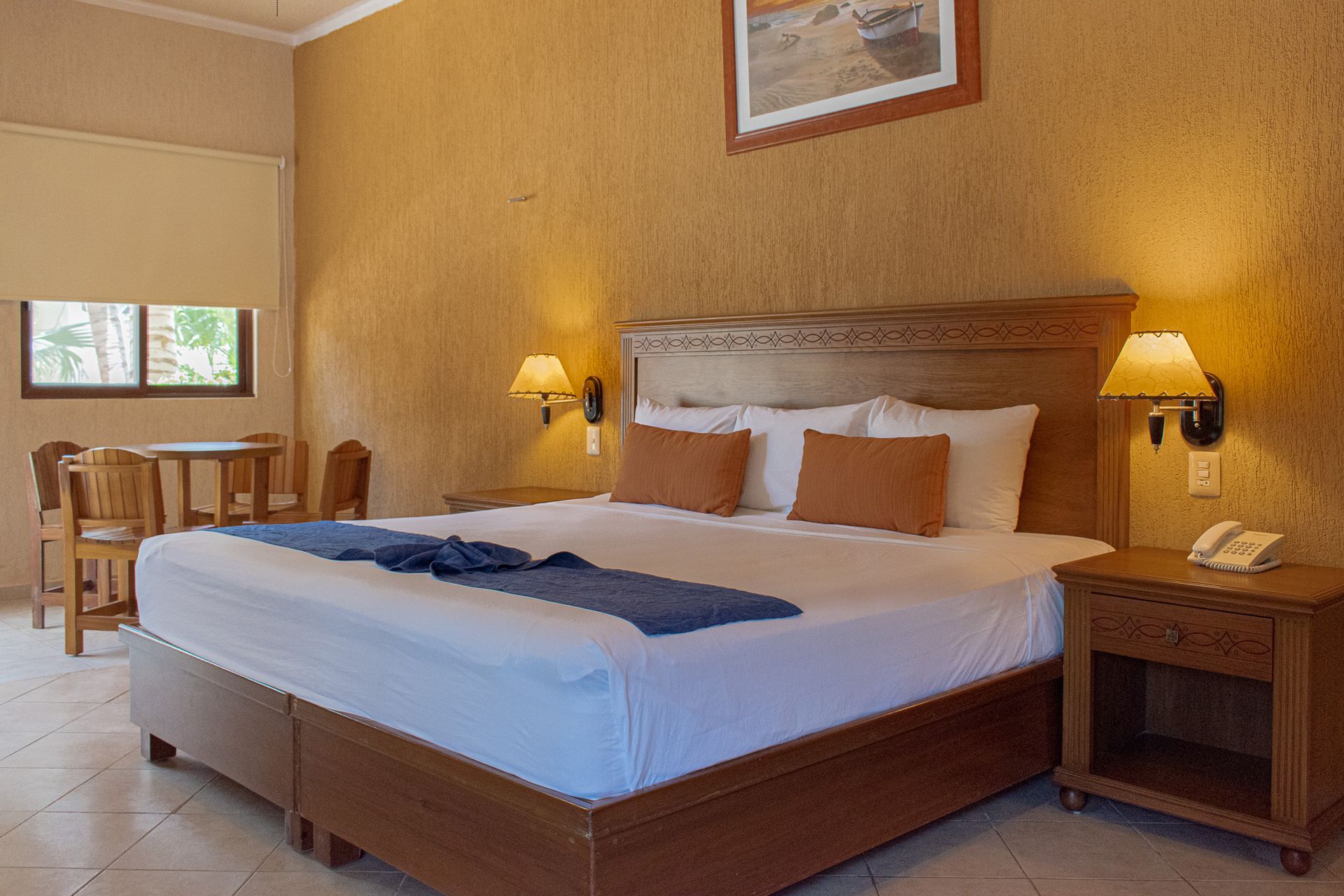 Una habitación de hotel con una cama king size, dos mesitas de noche, una mesa y sillas.