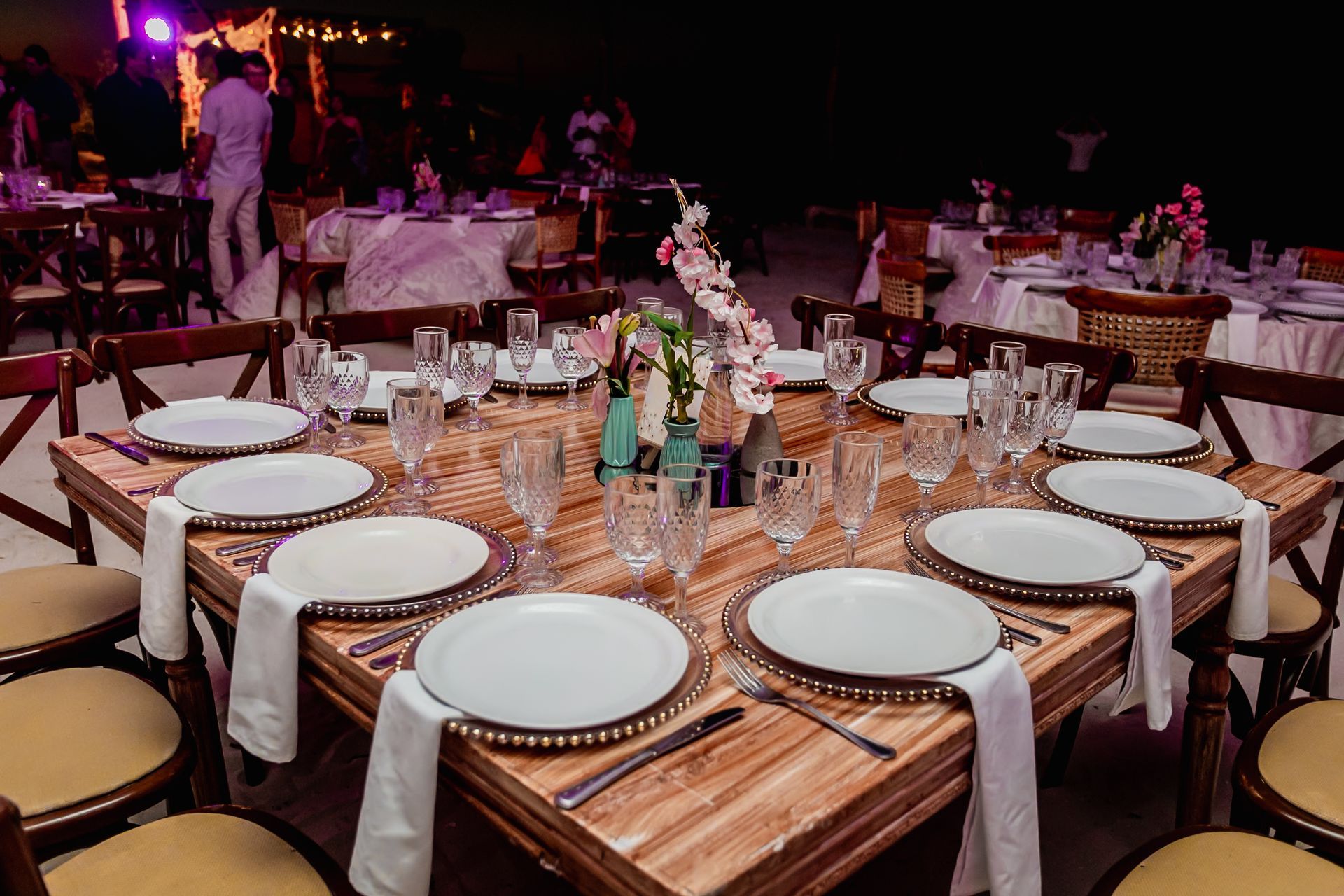 Una mesa preparada para una recepción de boda con platos, vasos y servilletas.
