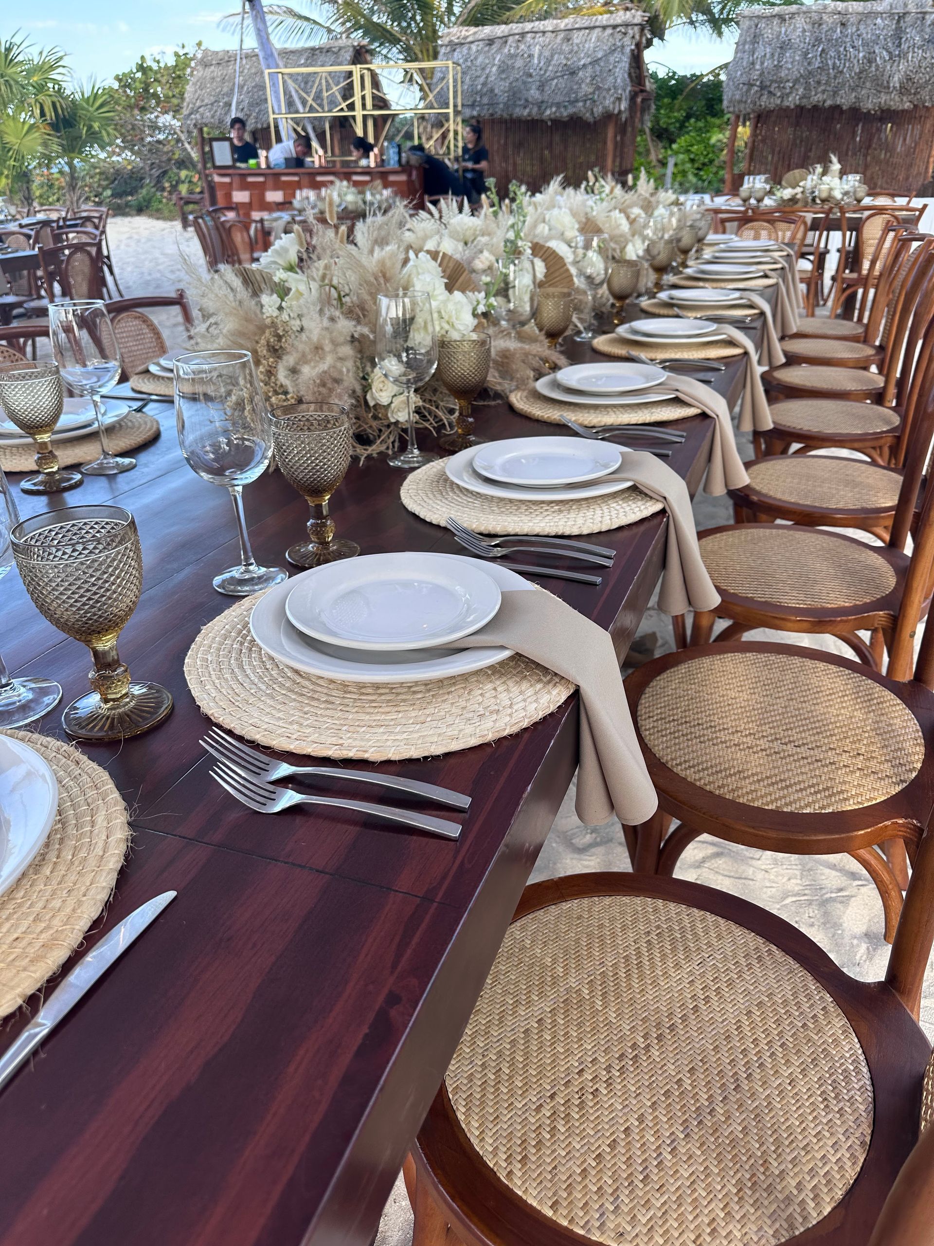 Una mesa larga de madera con platos, vasos, utensilios y flores sobre ella.
