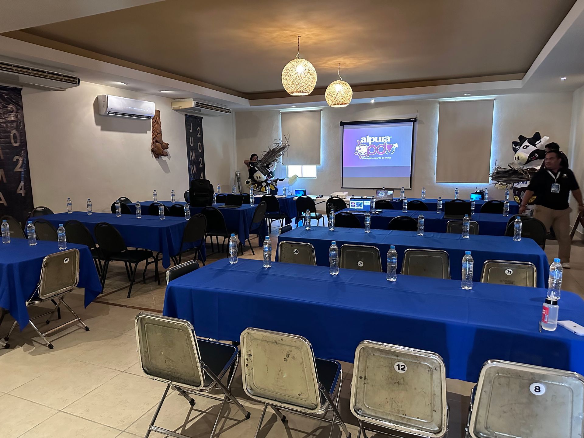 Una sala llena de mesas y sillas y una pantalla de proyector en Tecnohotel Beach.