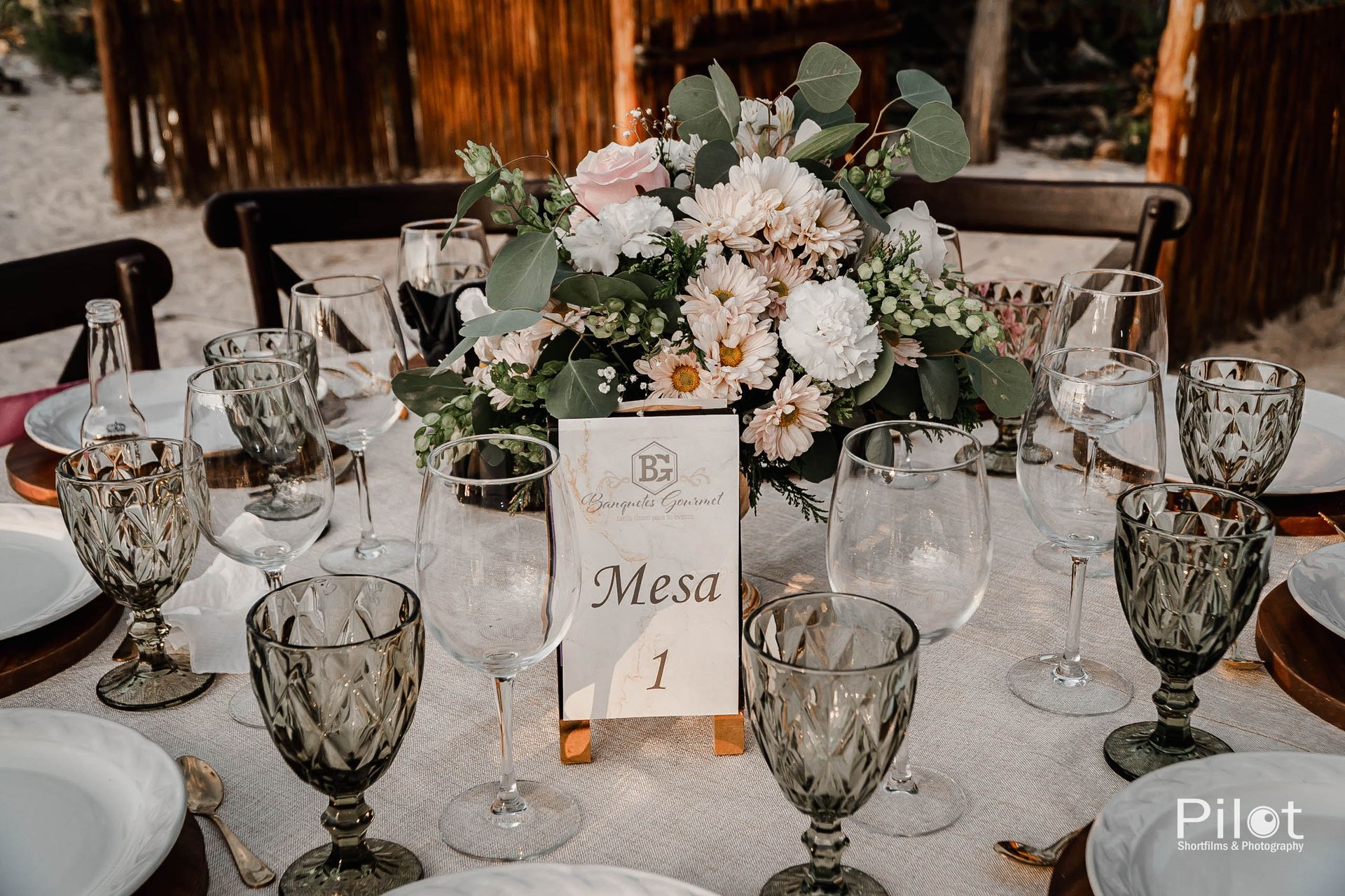 Una mesa con platos, copas de vino y un jarrón con flores sobre ella.
