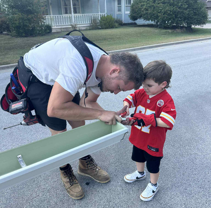 A man and a little boy are working on a gutter