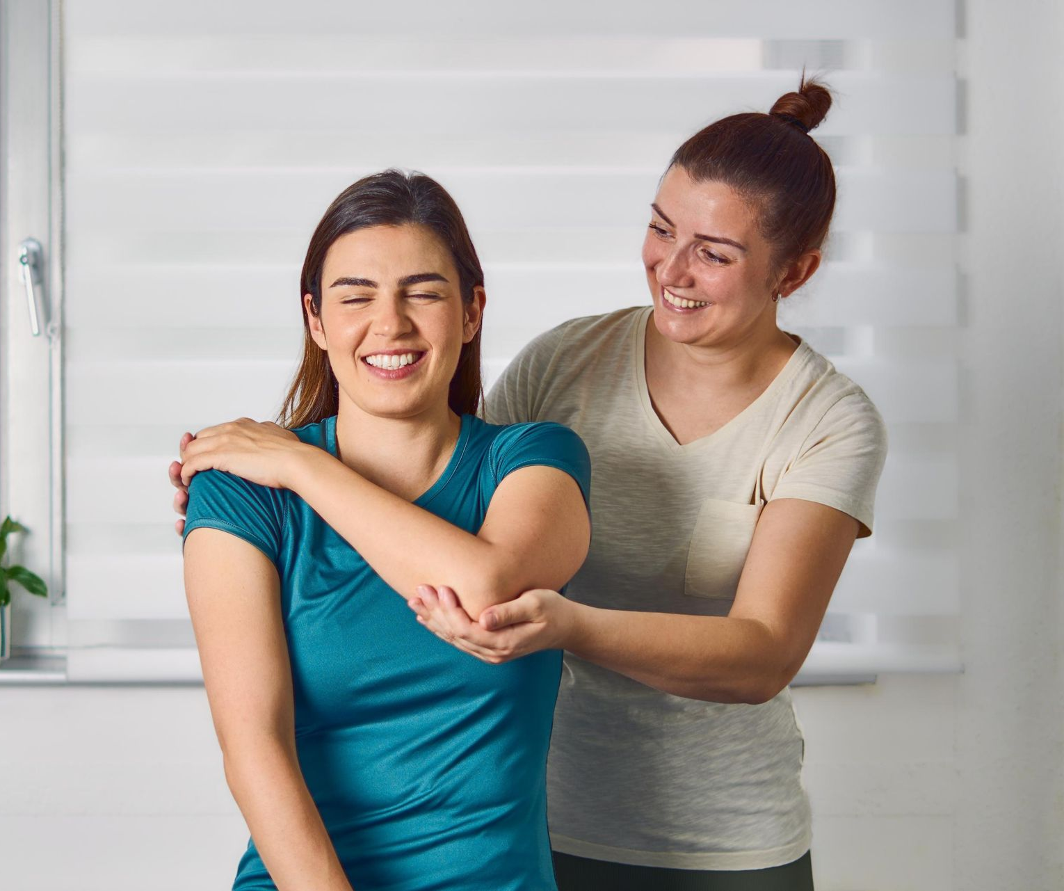Two women smiling while stretching together in a bright room