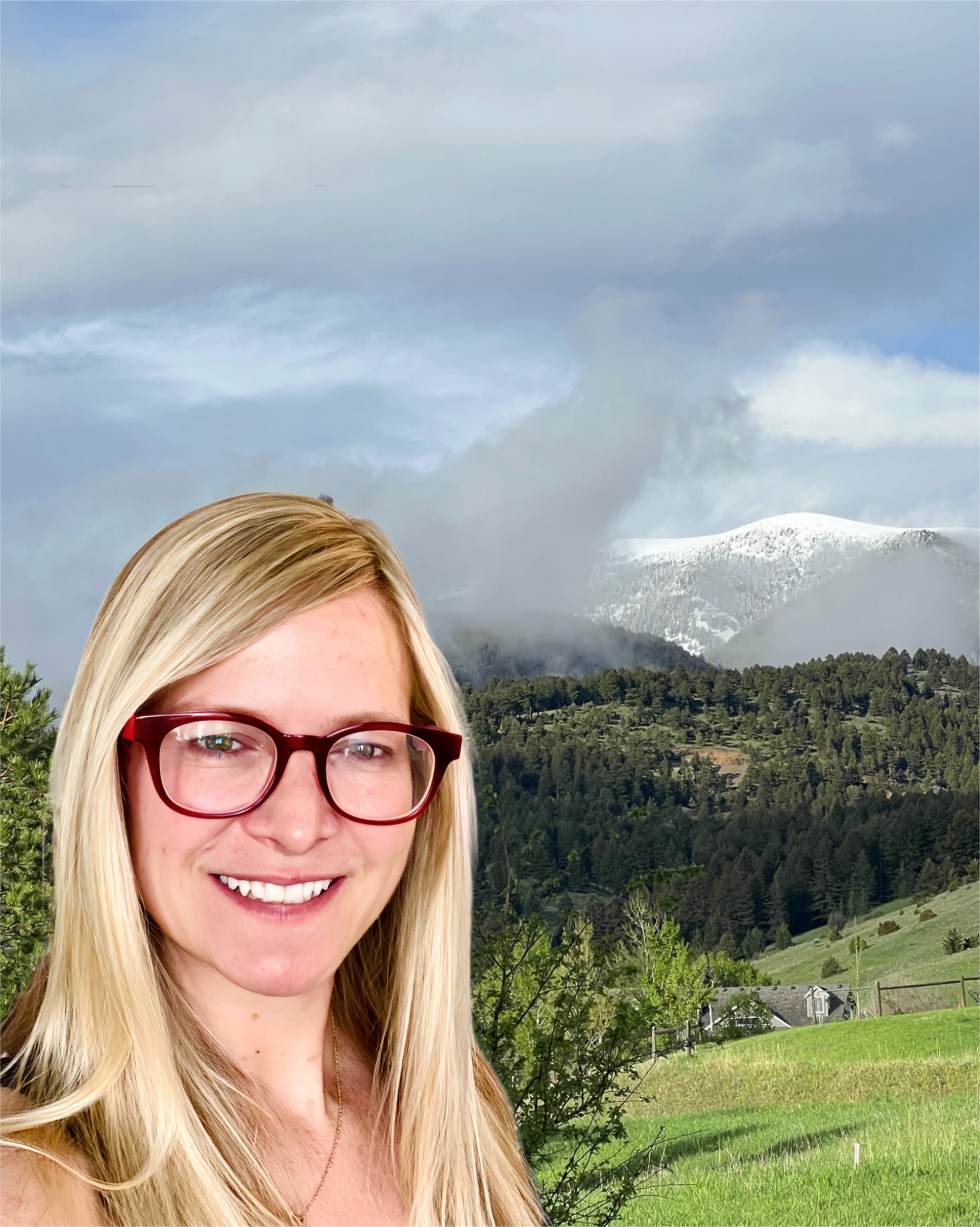 A woman wearing glasses is smiling in front of a mountain.