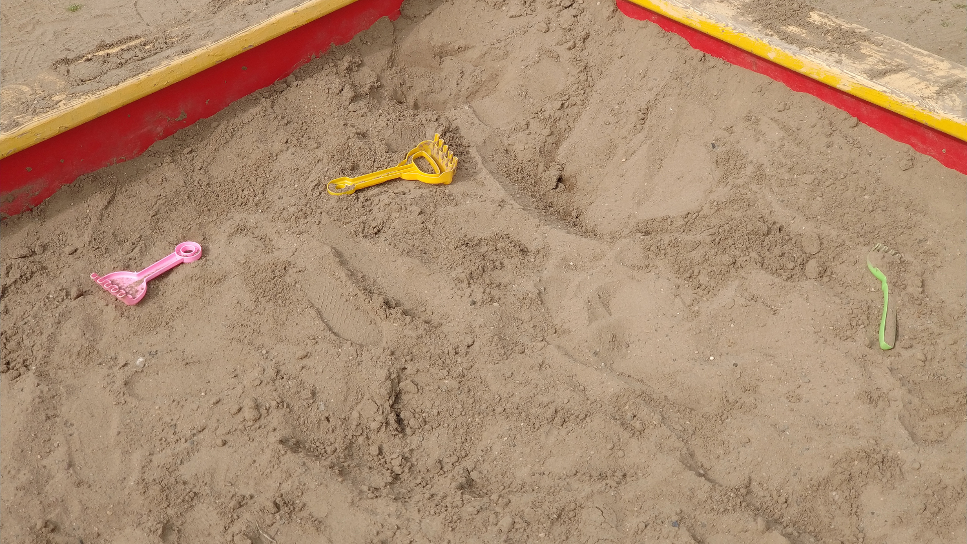 A sandbox with a yellow shovel and a pink spoon in it.