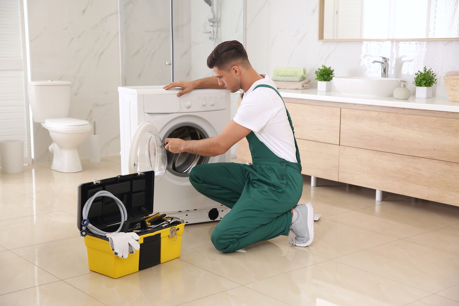 A man is fixing a washing machine in a bathroom.