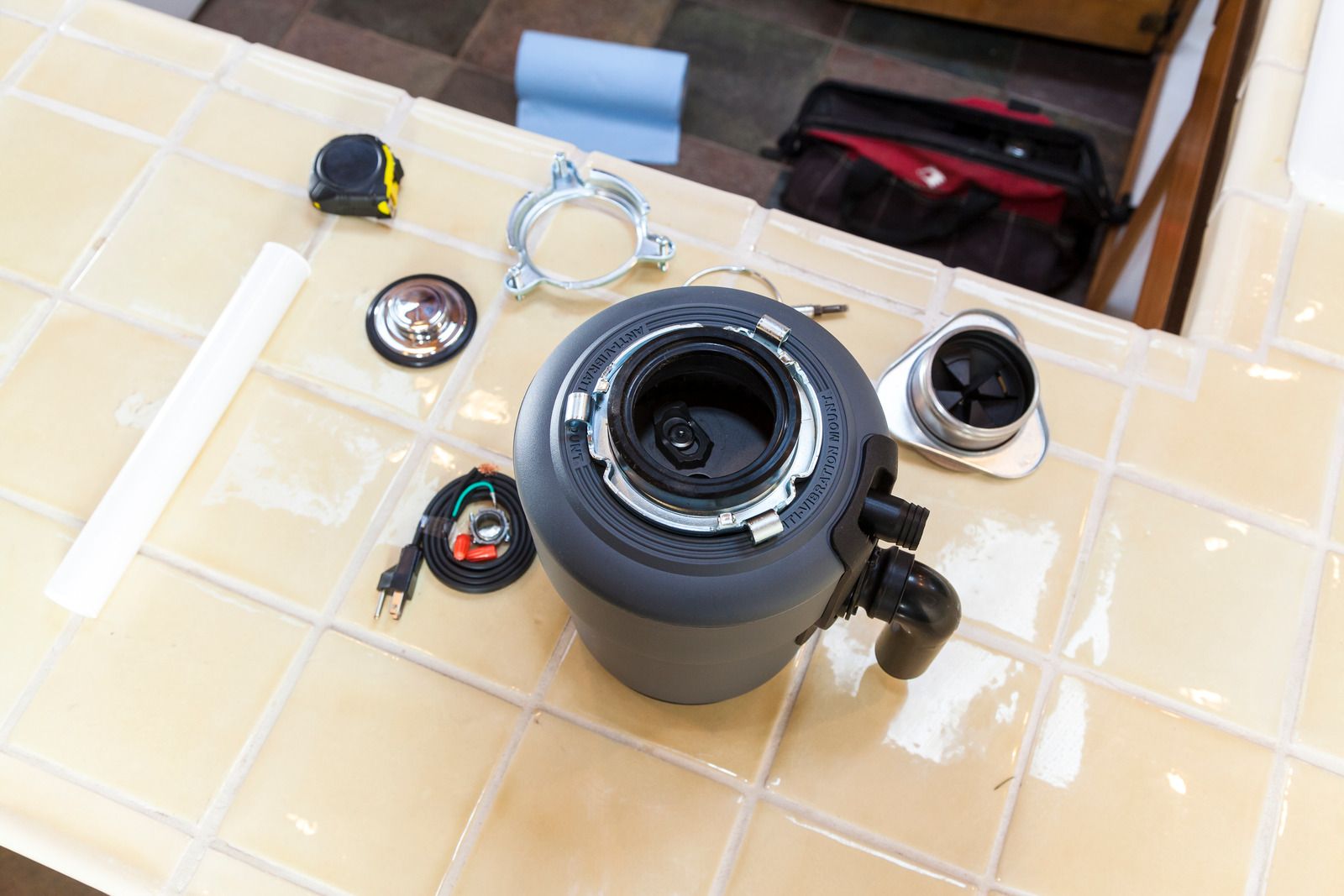 A garbage disposal is sitting on top of a tiled counter.