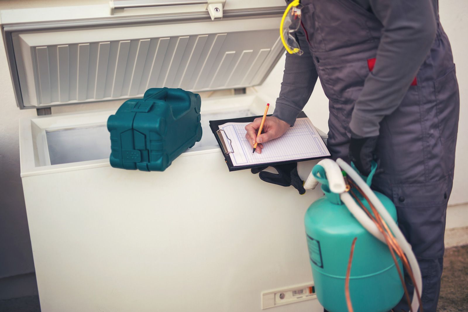 A man is standing next to a freezer and writing on a clipboard.