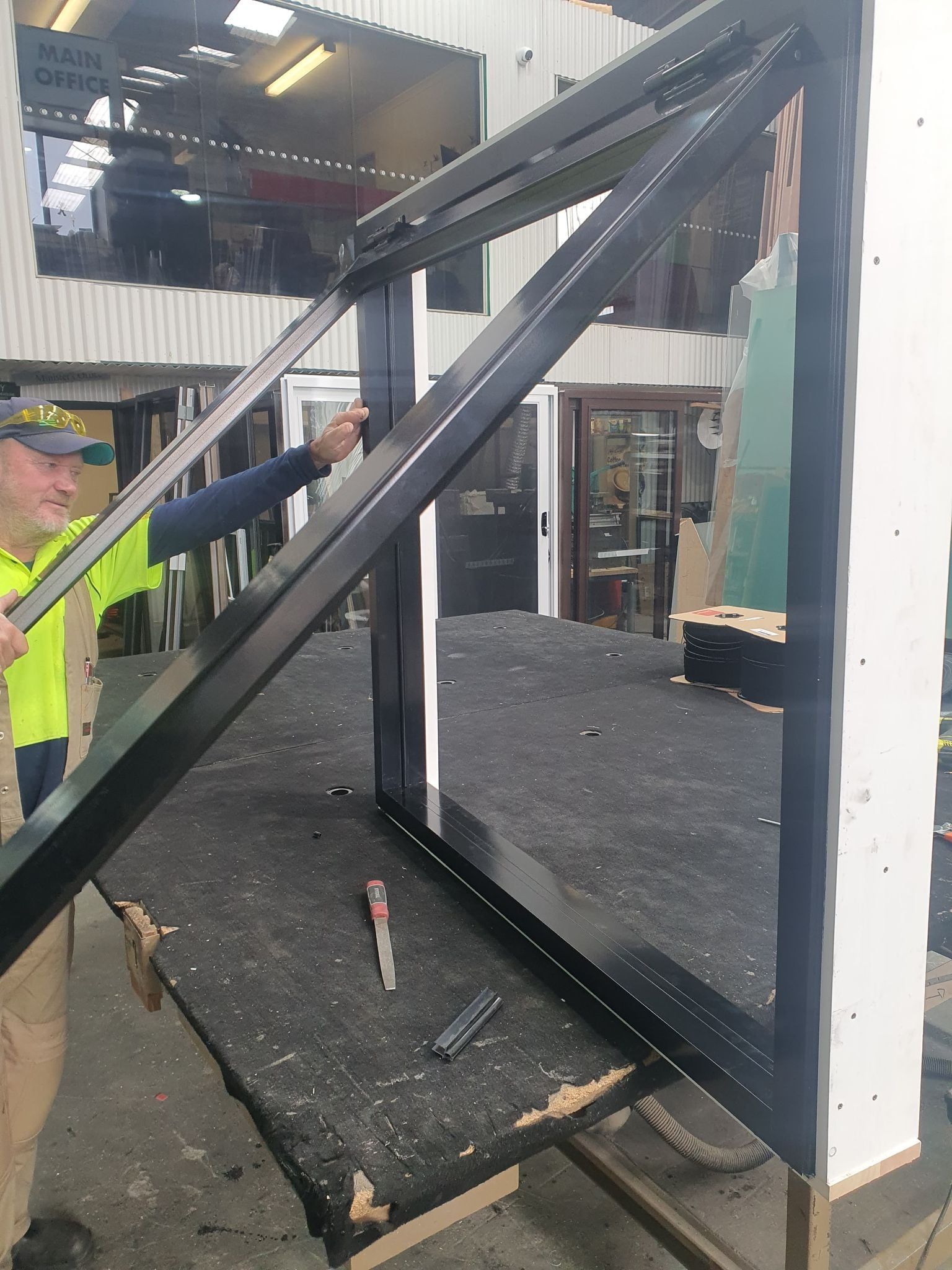 A Person in a High-visibility Vest Holds an Open Black Metal Window Frame — Channel Glazing In Electrona, TAS
