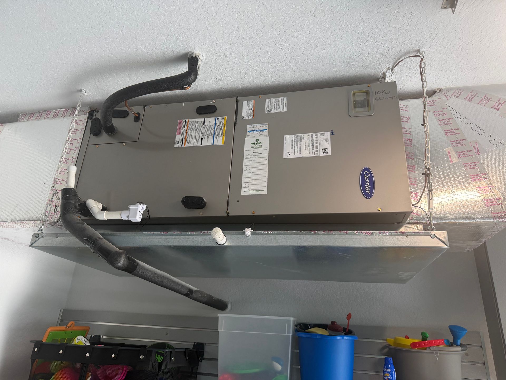 Wall-mounted HVAC unit with exposed black hoses above storage bins and metal ductwork.