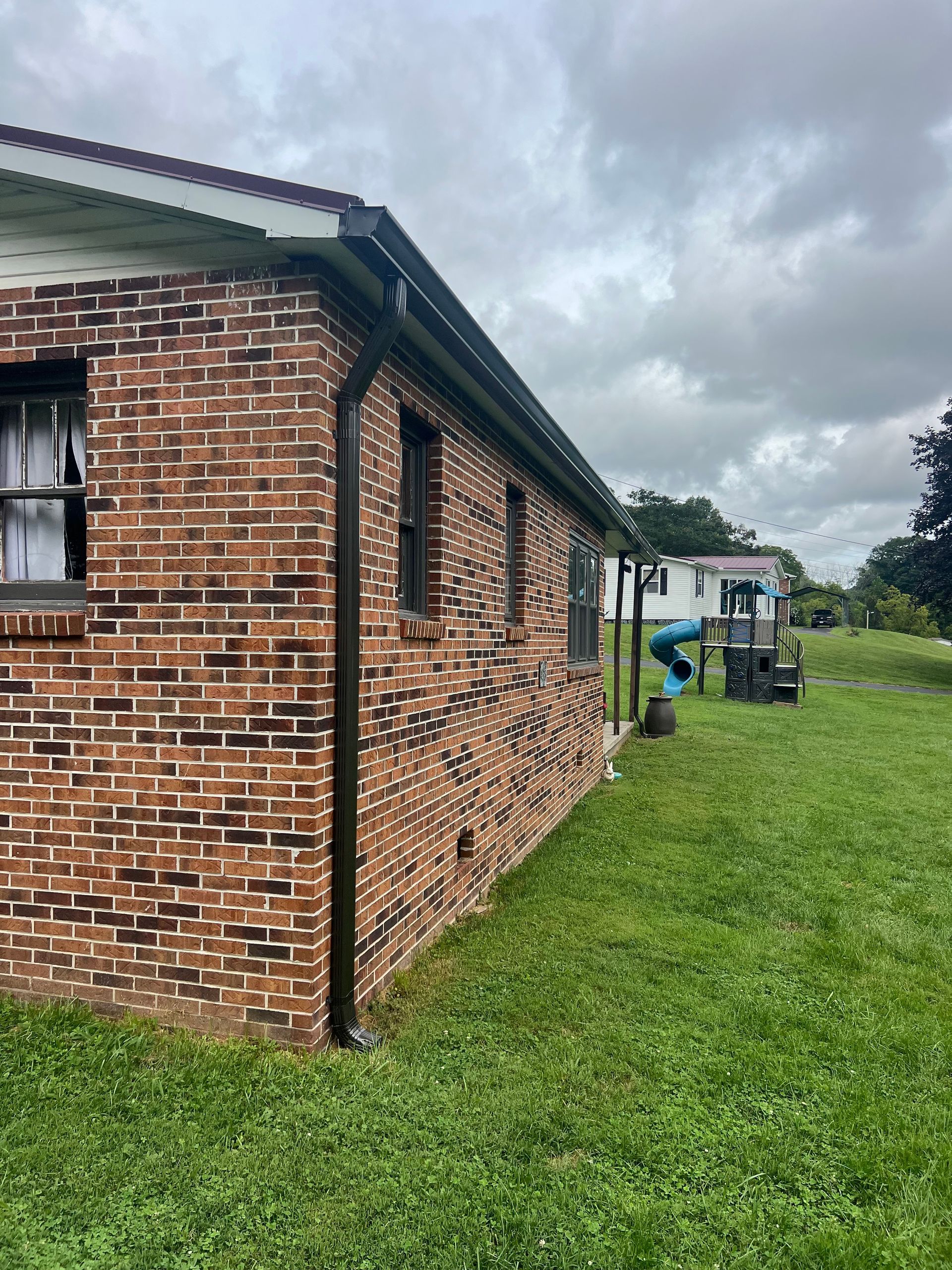 Brick house exterior with dark gutters, two windows, and a green lawn. Overcast sky.