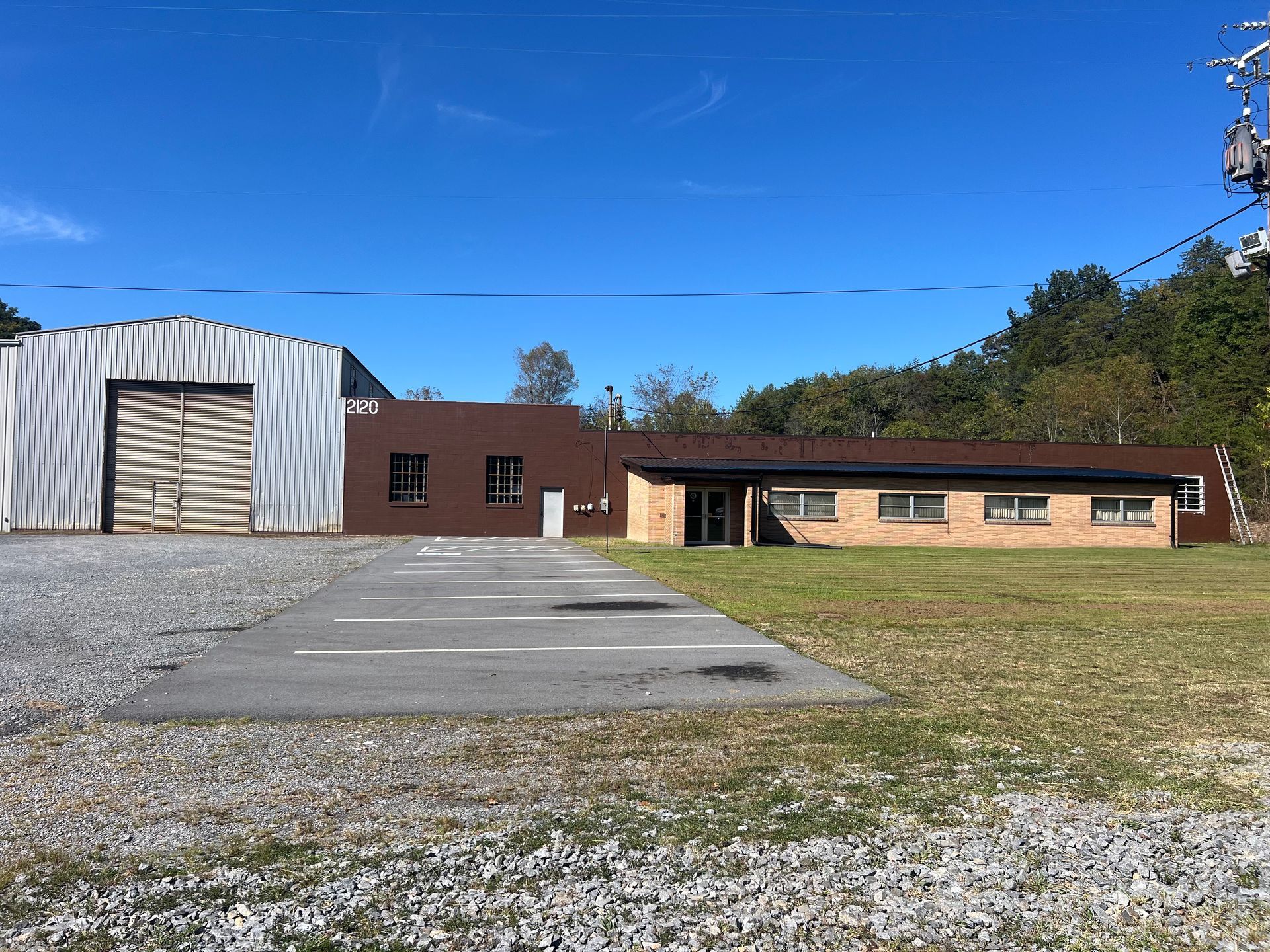 A commercial building with a light-colored metal warehouse and a brown brick building. Blue sky.