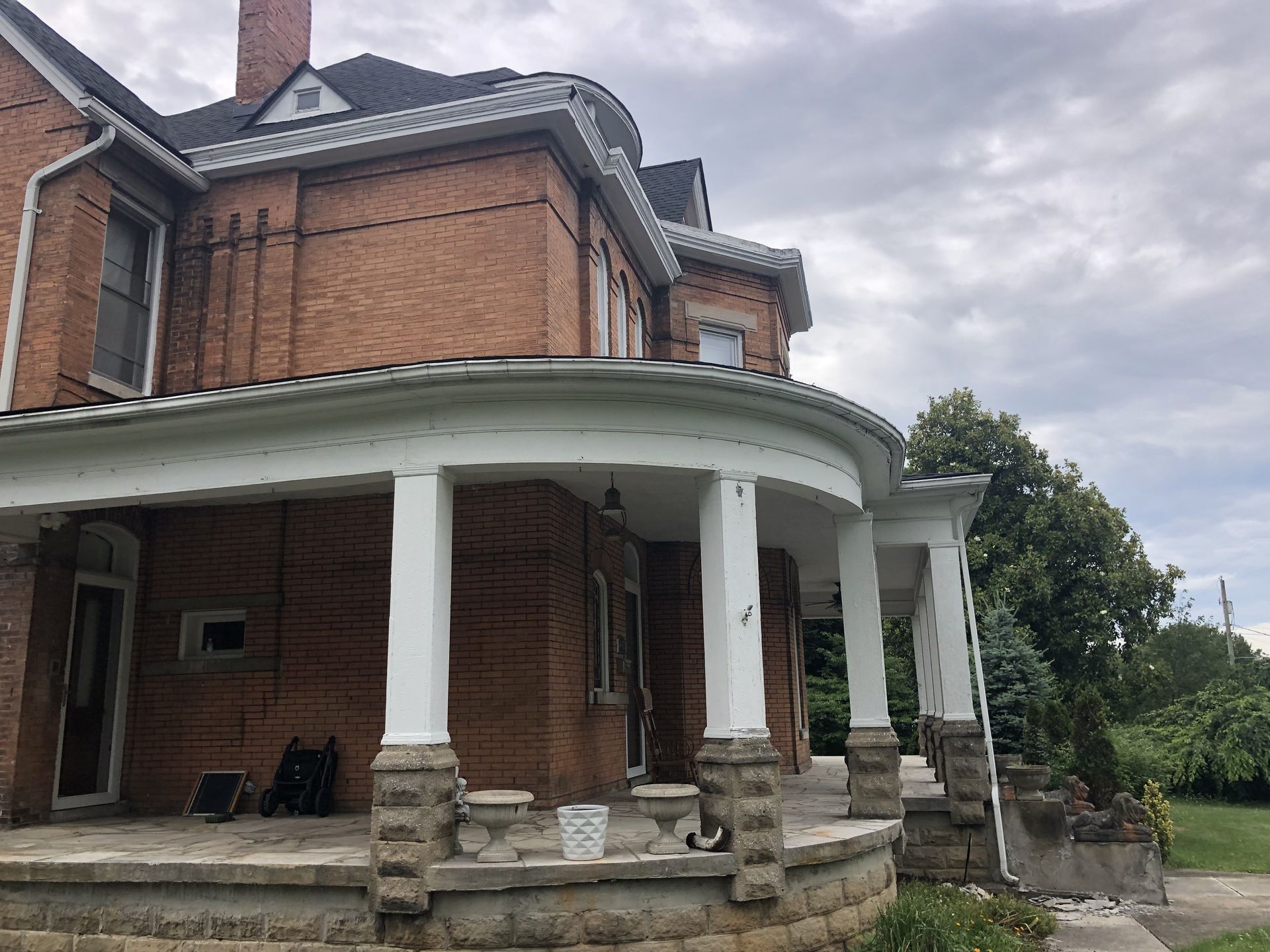 Brick house with a curved porch and columns, cloudy sky.