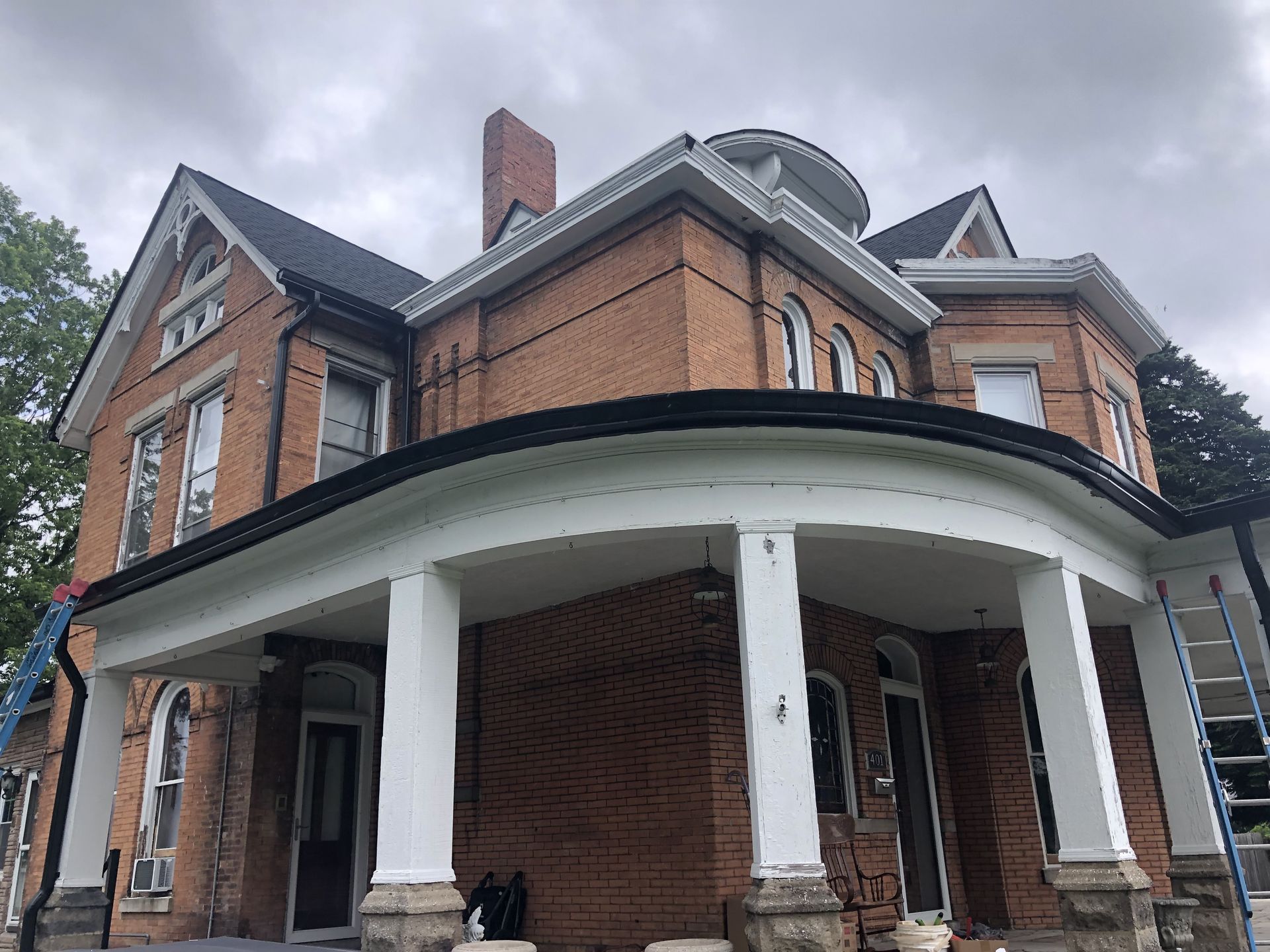 Red brick house with white columns and black roof under overcast sky.