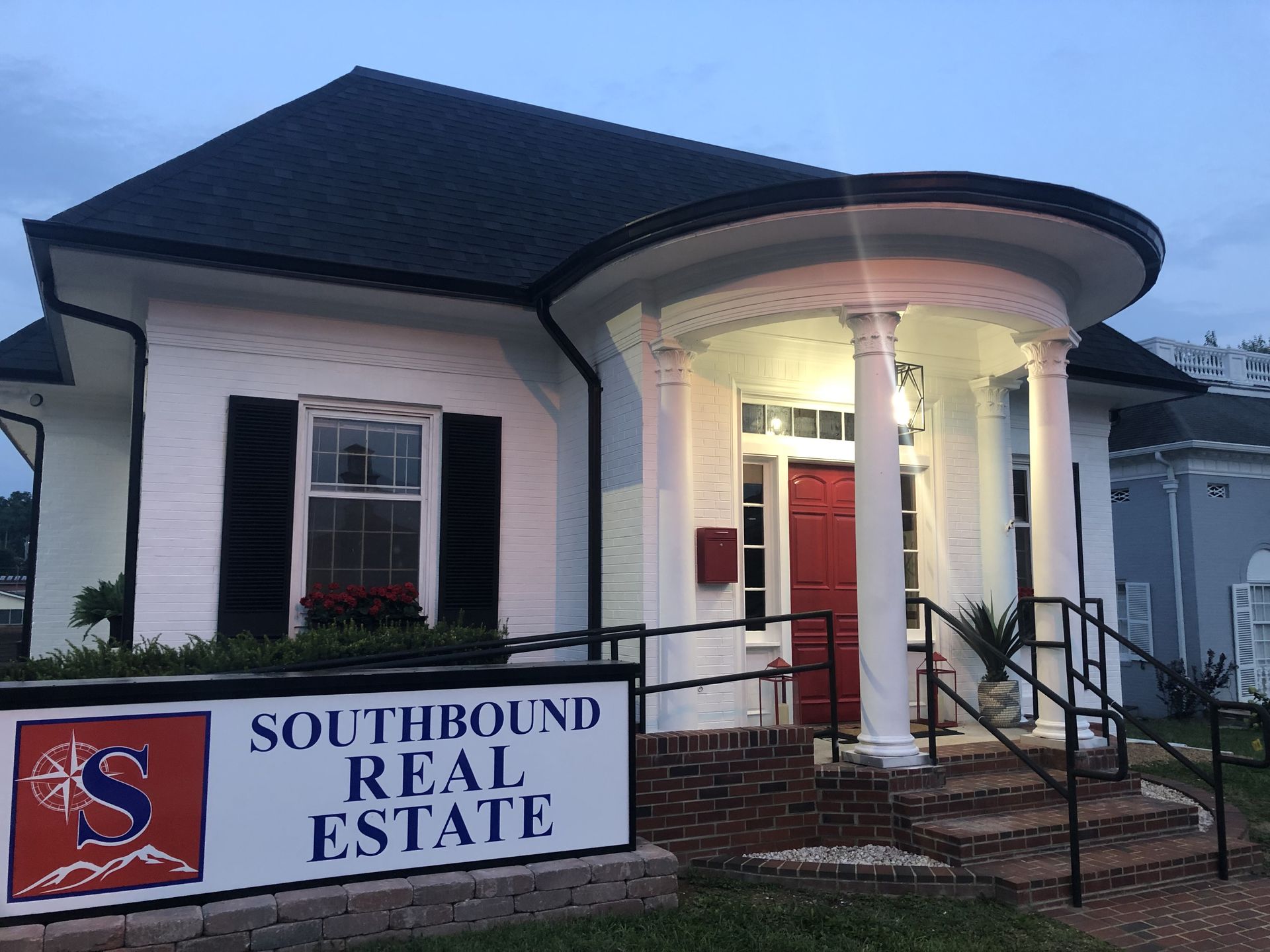 Southbound Real Estate office with white exterior, red door, and sign at dusk.