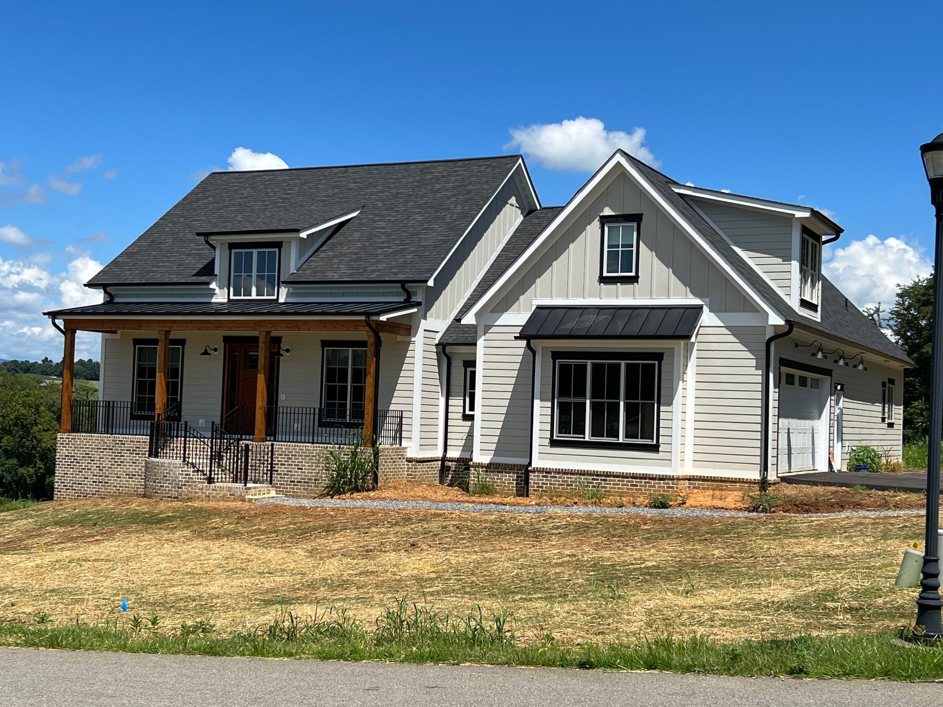 Two-story house with gray siding, black accents, and a porch, on a grassy hill under a blue sky.
