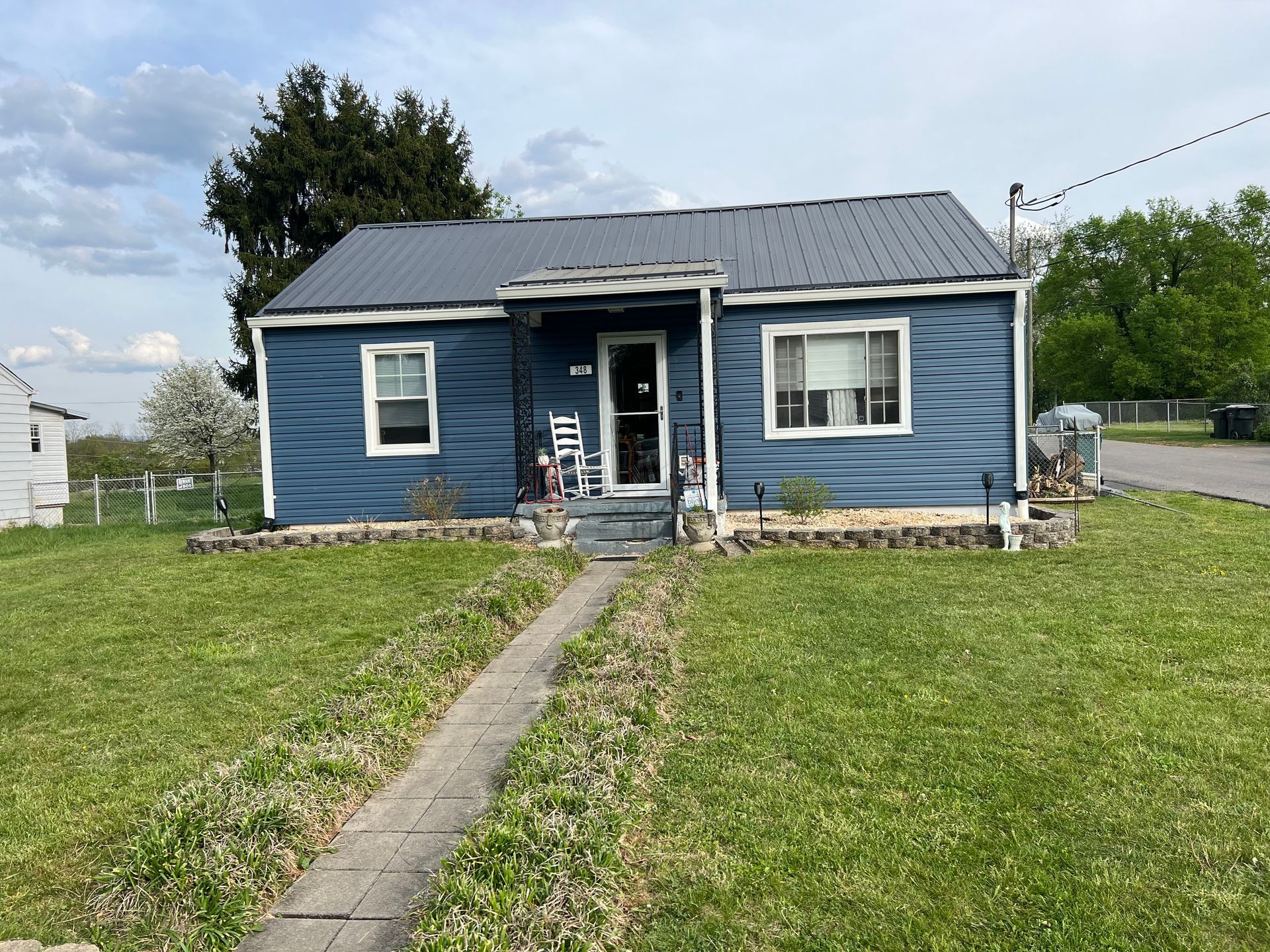 Blue house with a metal roof and a small porch on a grassy lawn.