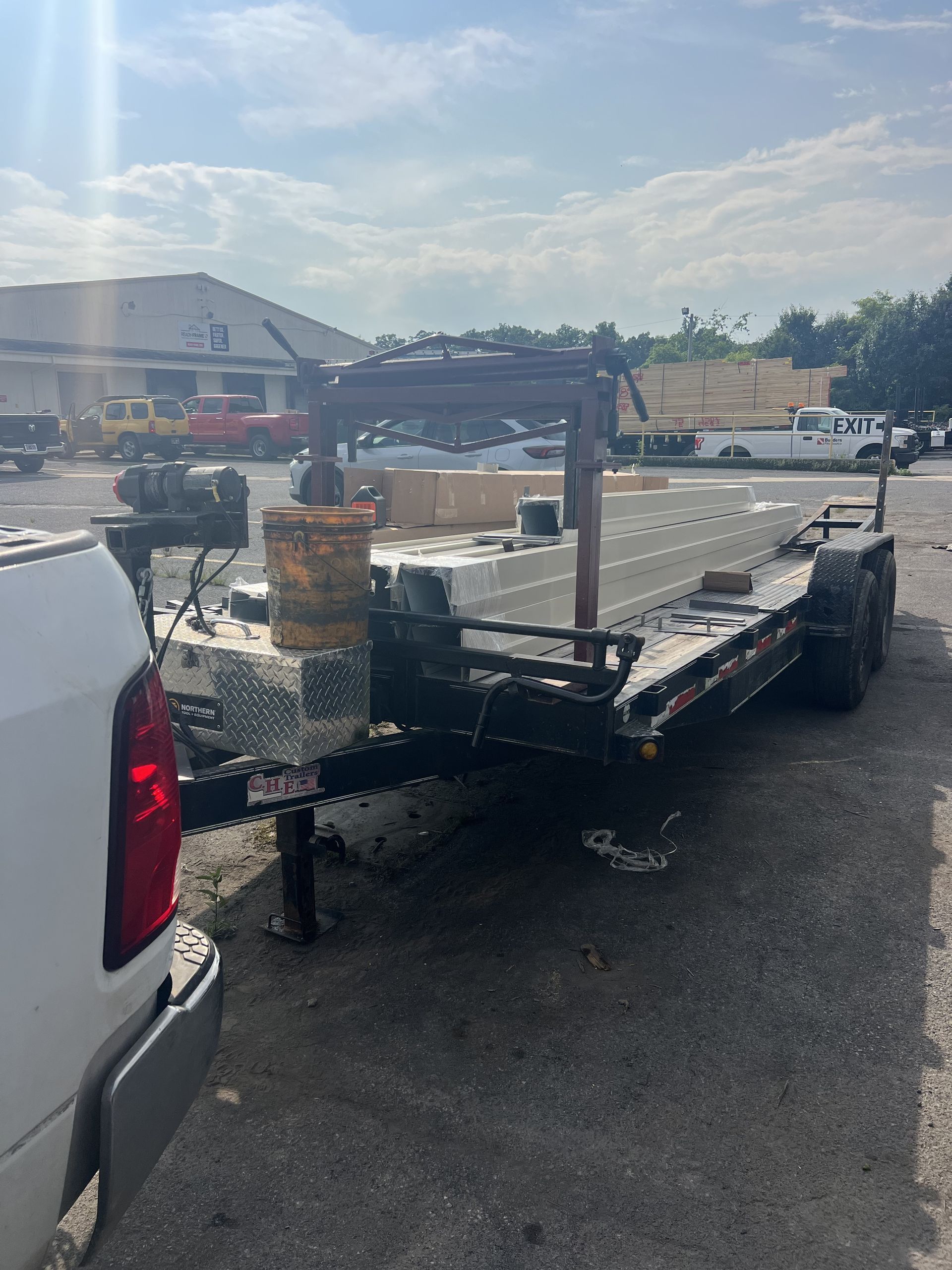 Black trailer loaded with lumber, hooked to a white truck, parked in a lot.