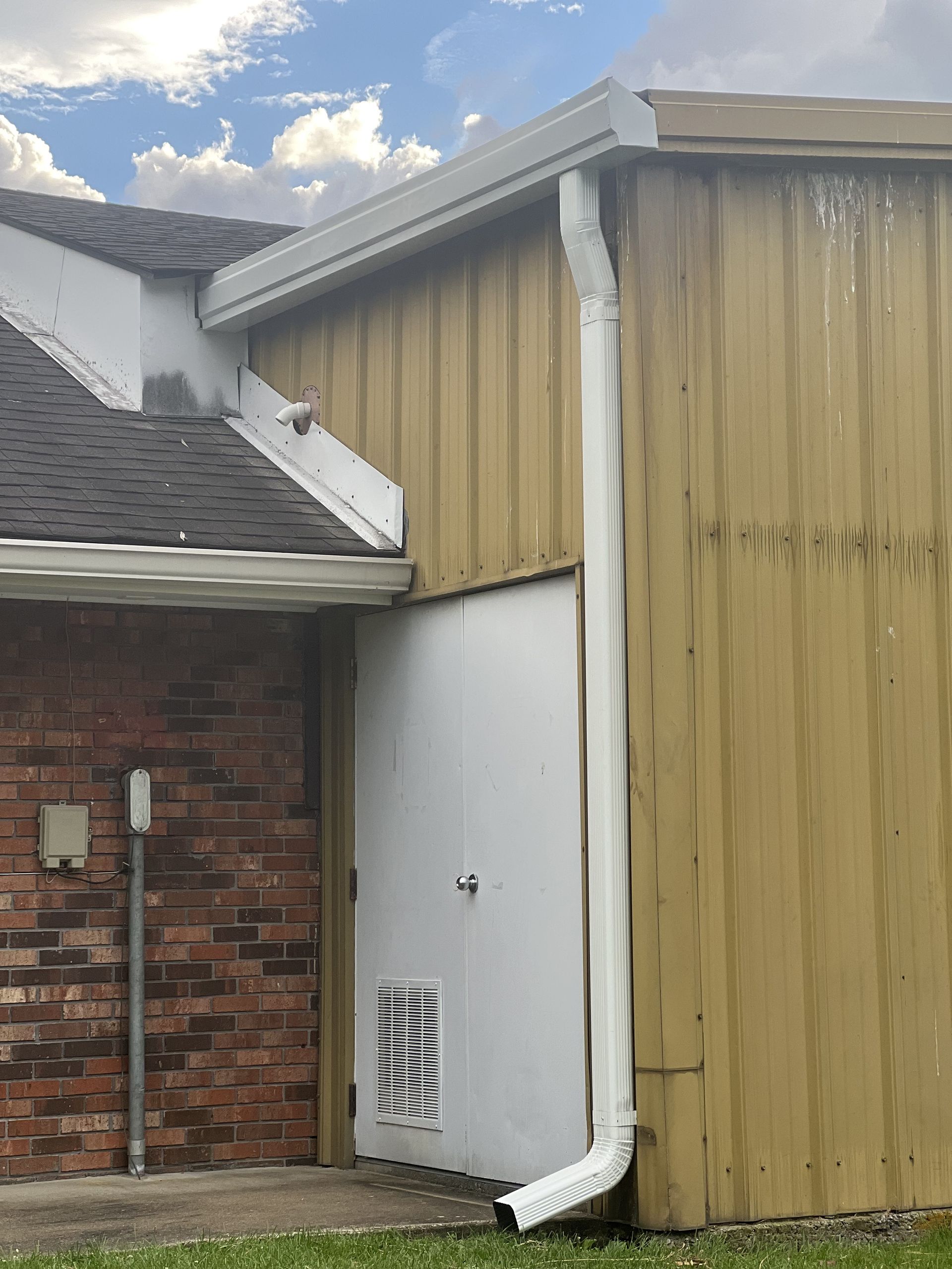Exterior of a building with white gutters, a downspout, and a white door on a yellow wall.