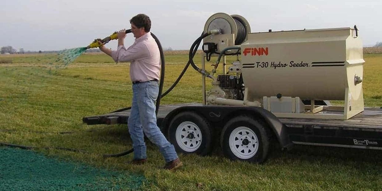 Man spraying green material onto grass with machine on trailer