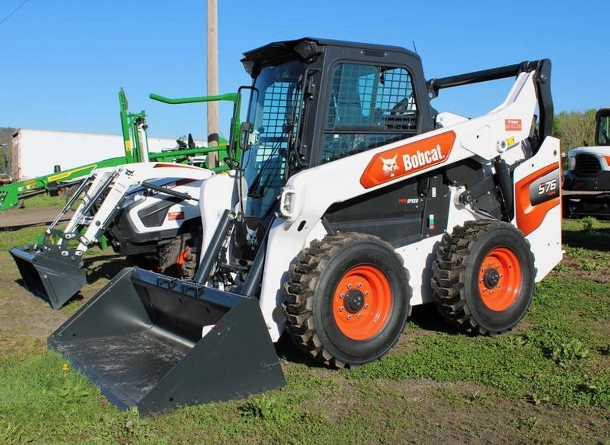 White and orange Bobcat skid-steer loader with a bucket, parked on grass