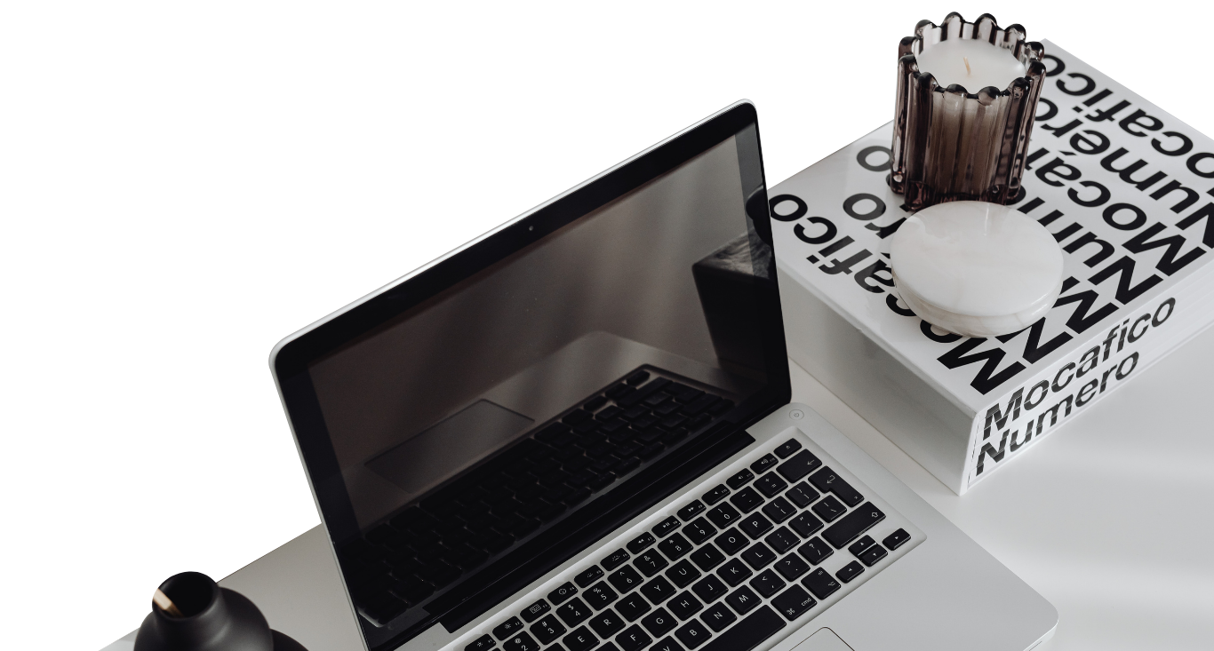 Laptop next to a white pastry box with a chocolate cake on a white desk