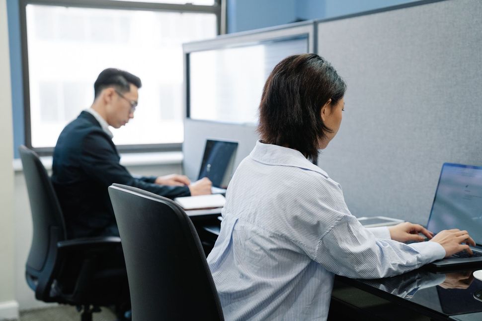 Two coworkers typing on laptops in a modern office cubicle area