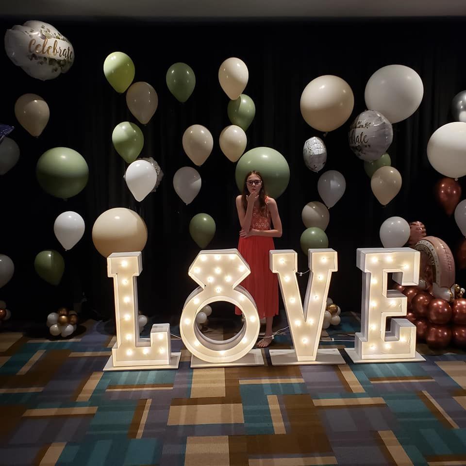 A woman stands in front of a large lighted love sign