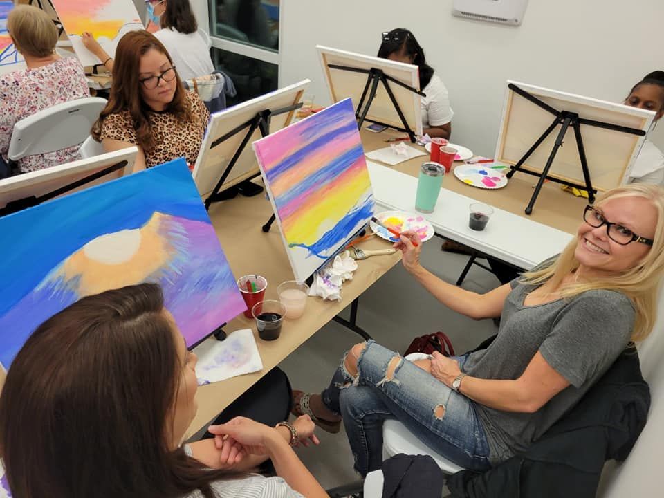 A group of women are sitting at a table painting.