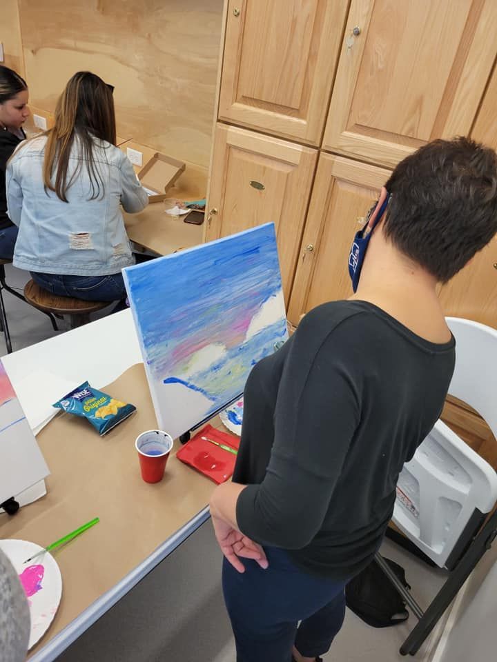 A woman is standing in front of a painting on a canvas.